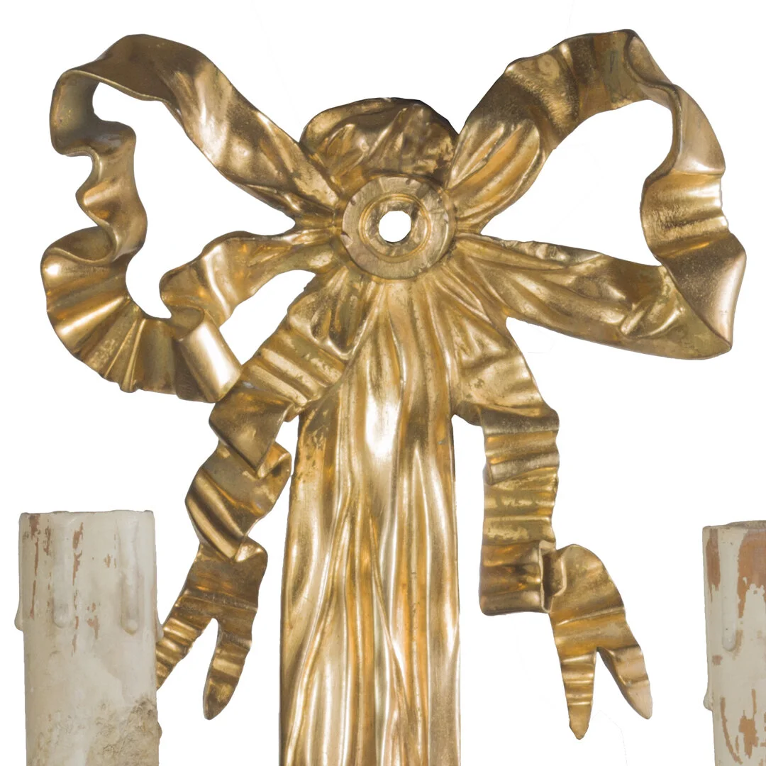 Decorative metallic gold bow with flowing ribbons, flanked by tall white candles with wax drippings.