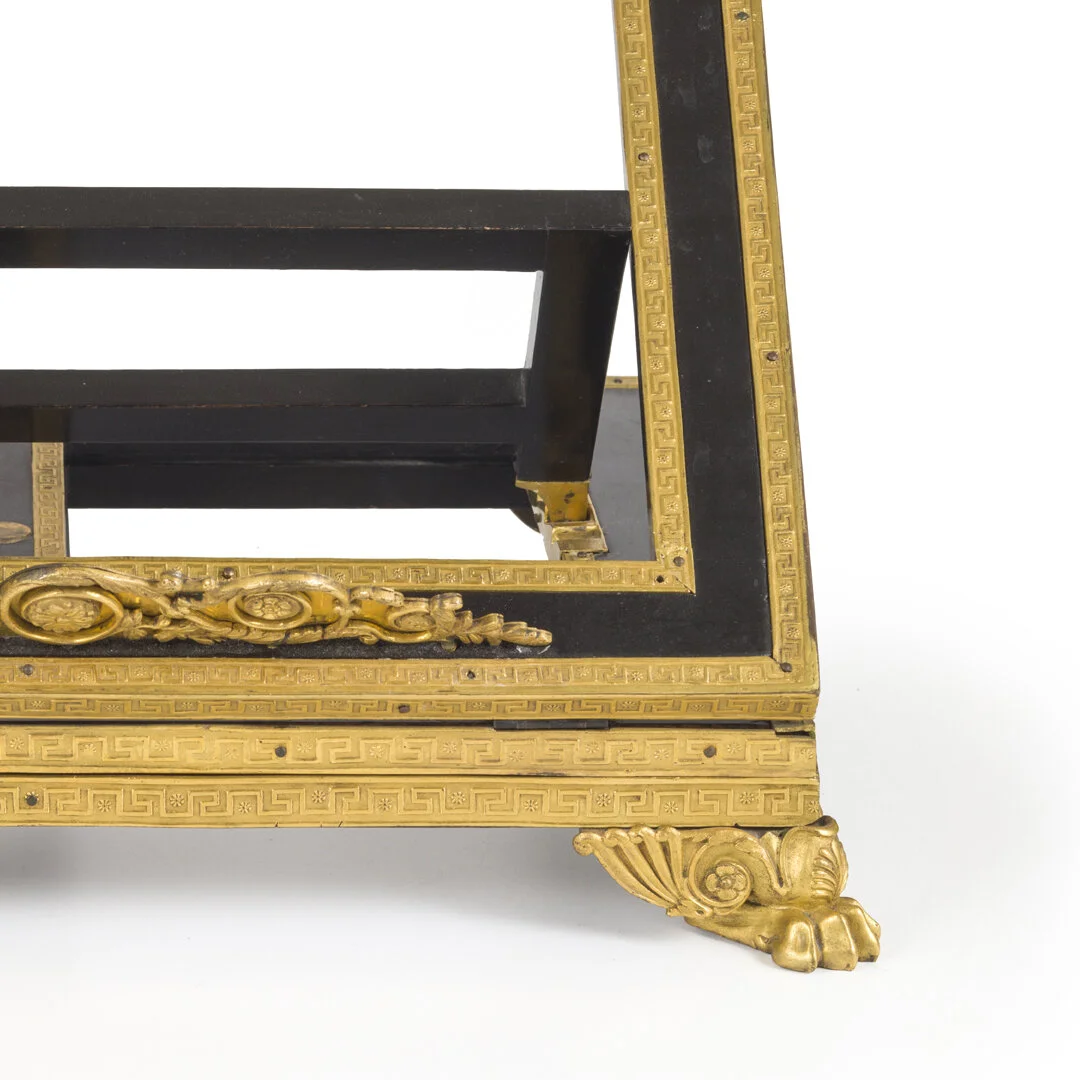 Close-up of an ornate furniture piece with gold and black detailing, including decorative gold elements, a black frame, and a paw-shaped gold foot.