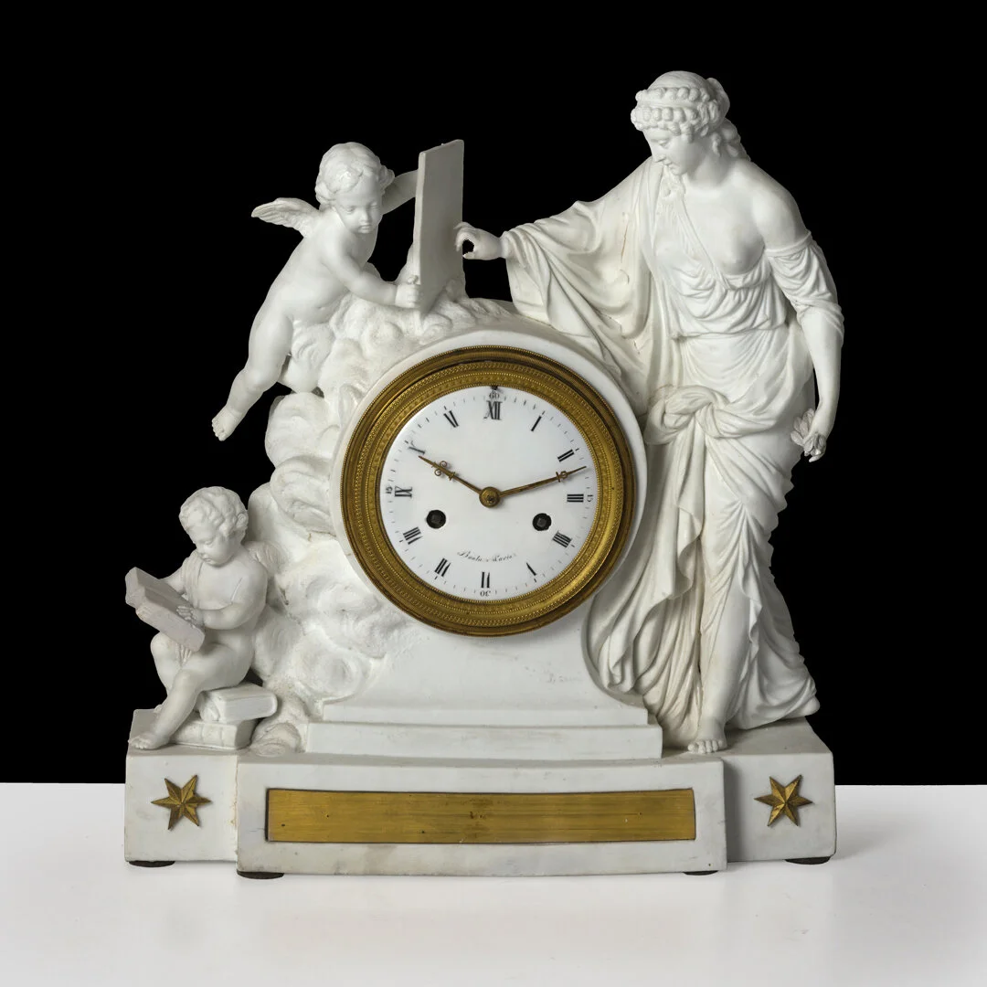 An ornate vintage clock integrated into a white sculptural base featuring three cherubs and a woman, with a black background.