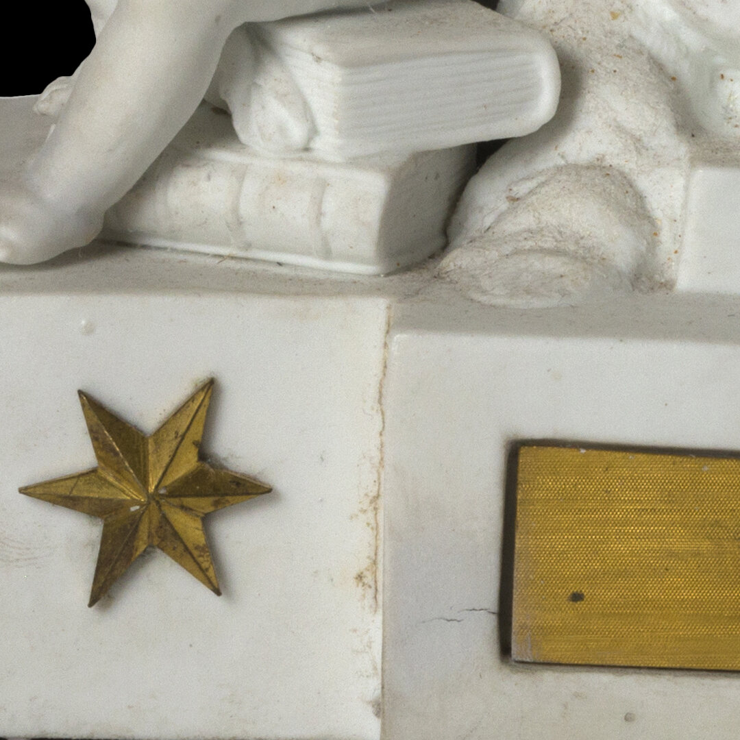 Close-up of a white ceramic or plaster decorative object featuring a gold star and a rectangular yellow label or plaque.
