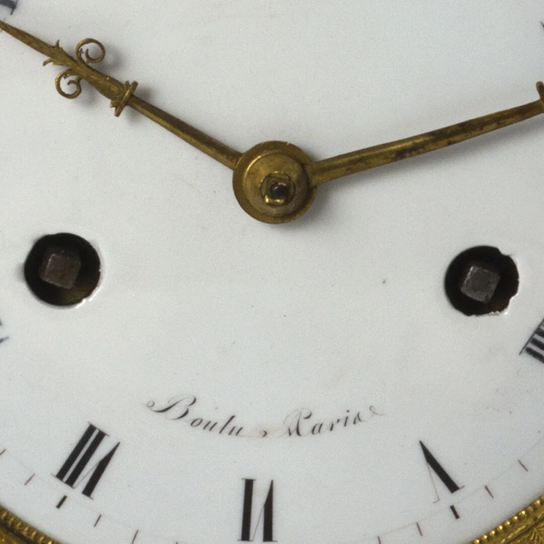 Close-up of a vintage clock face with Roman numerals and ornate gold hands, signed 'Bouler, Ravia'.