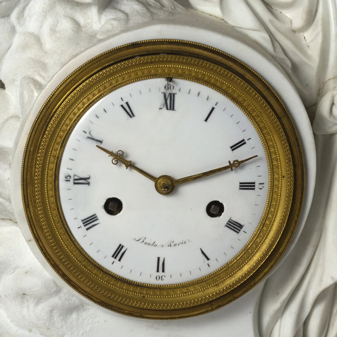 Close-up of an antique clock with Roman numerals, gold trim, and two winding holes.