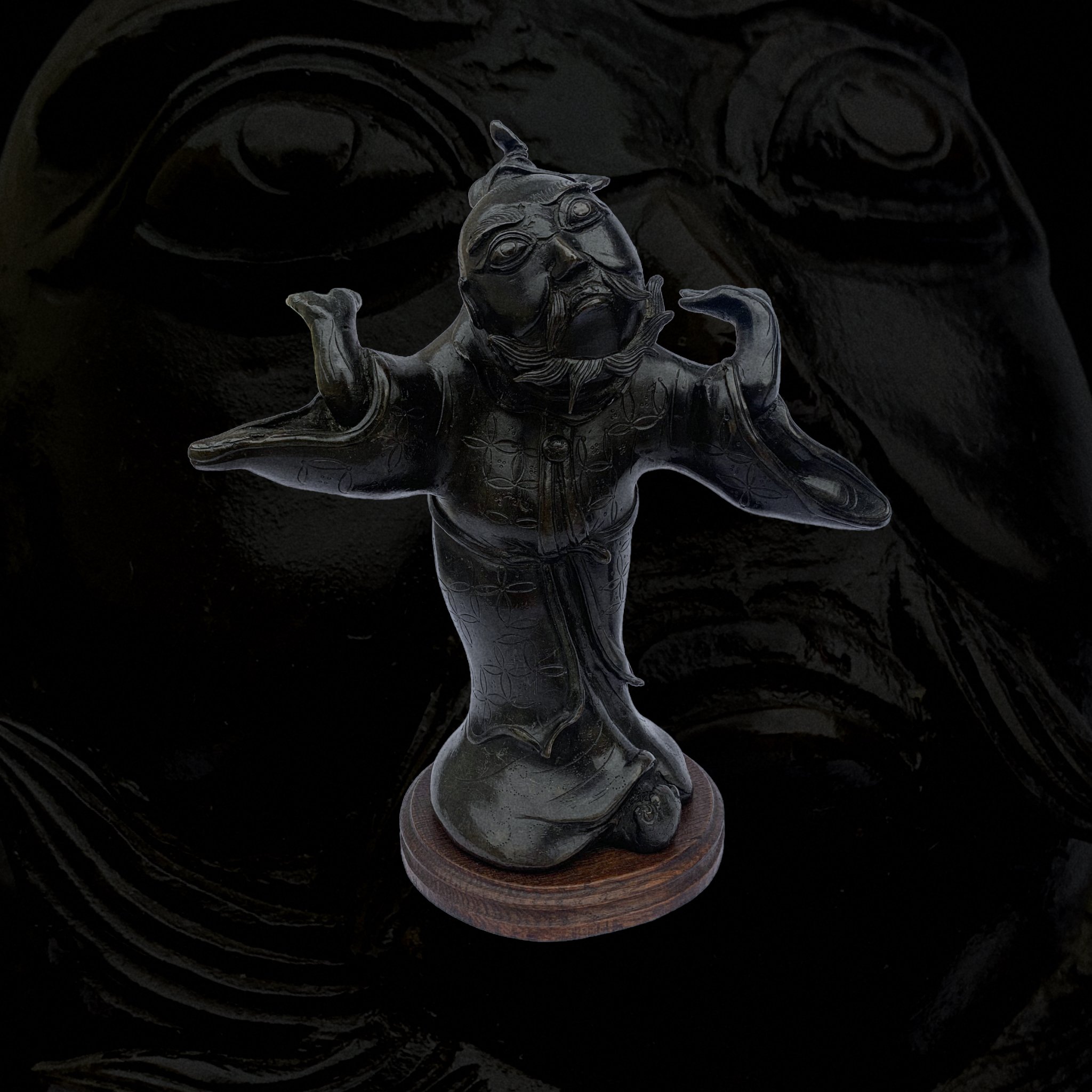 Dark-colored carved figurine of a mythical creature with a human face and animal body, mounted on a round wooden base.