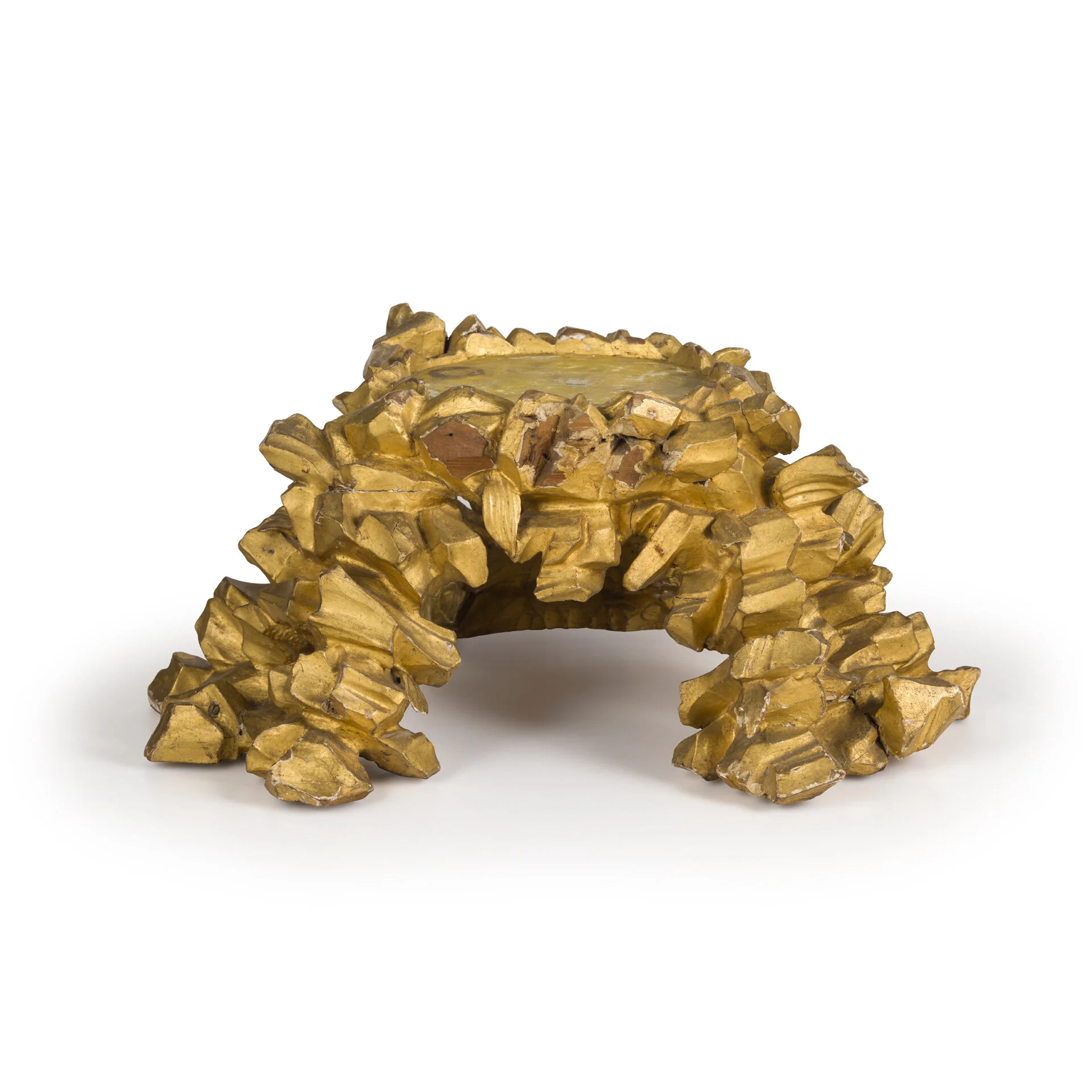 A gold decorative sculpture resembling a small arch or bridge, made of multiple irregular, angular pieces