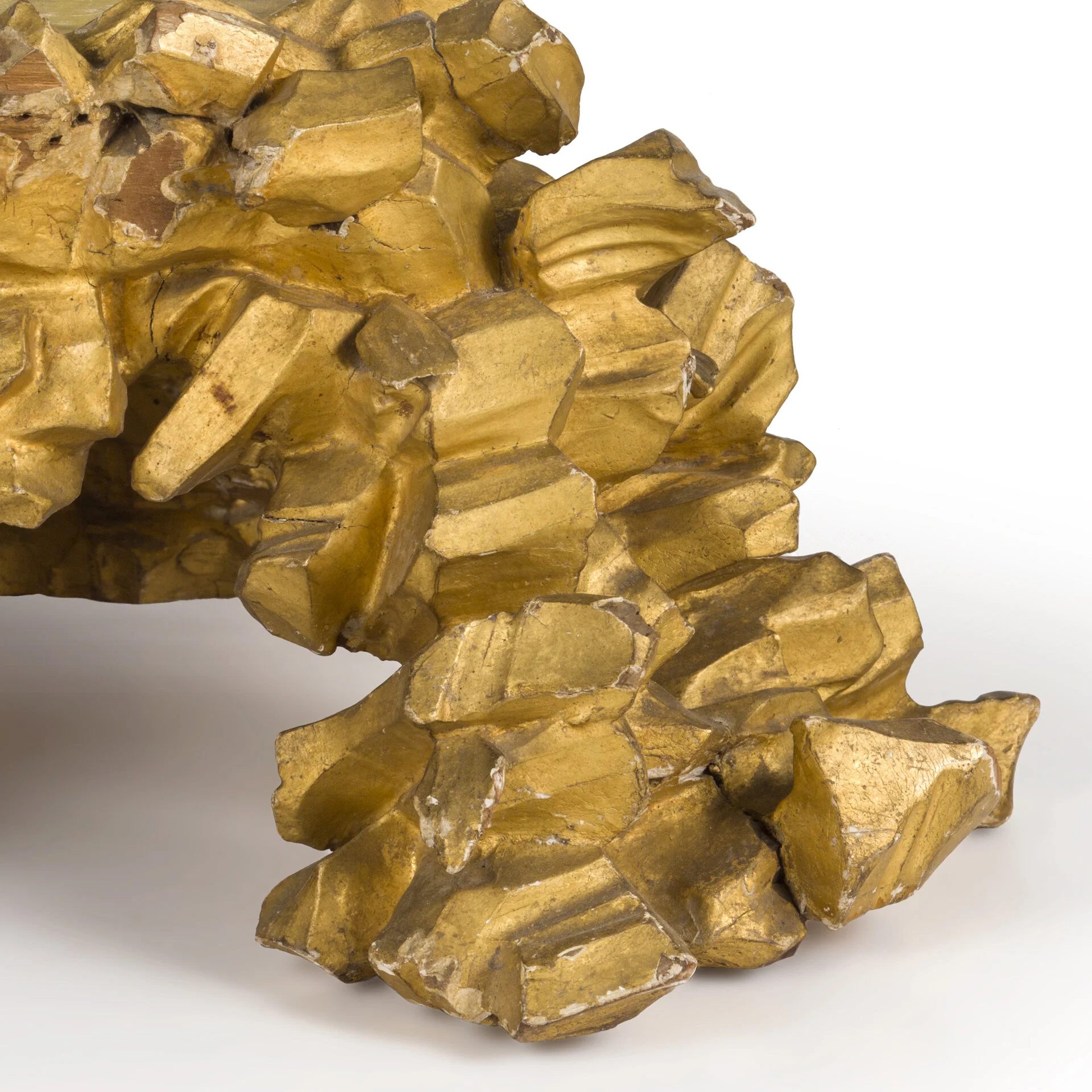 Close-up photograph of a cluster of gold-colored crystals with sharp edges, set against a light background.