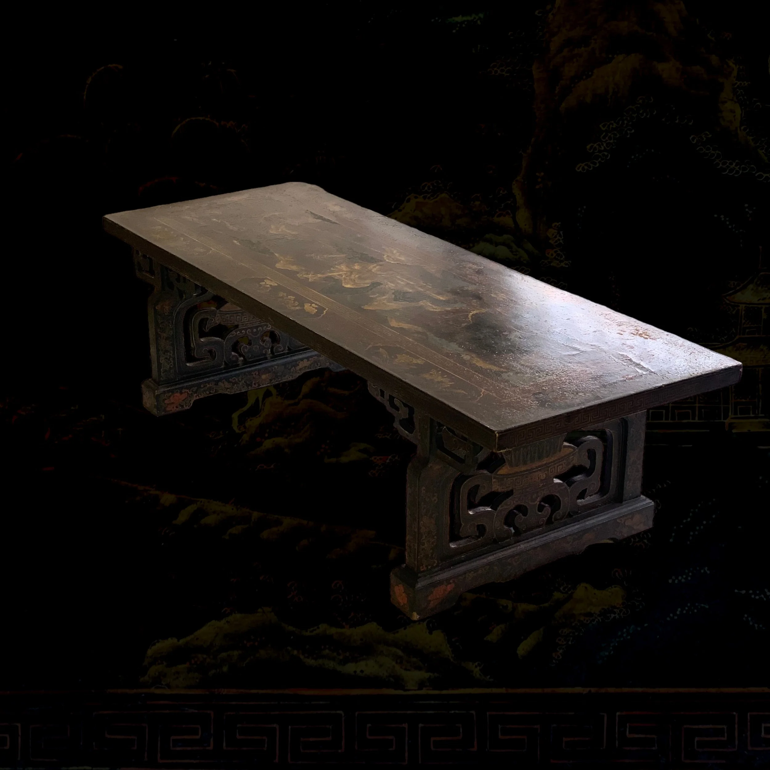 An antique wooden table with intricate carved legs and a weathered surface, set against a dark background with traditional Chinese landscape patterns.