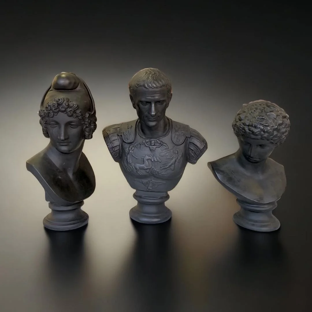Three classical bust sculptures of historical figures on a black surface with a dark background.