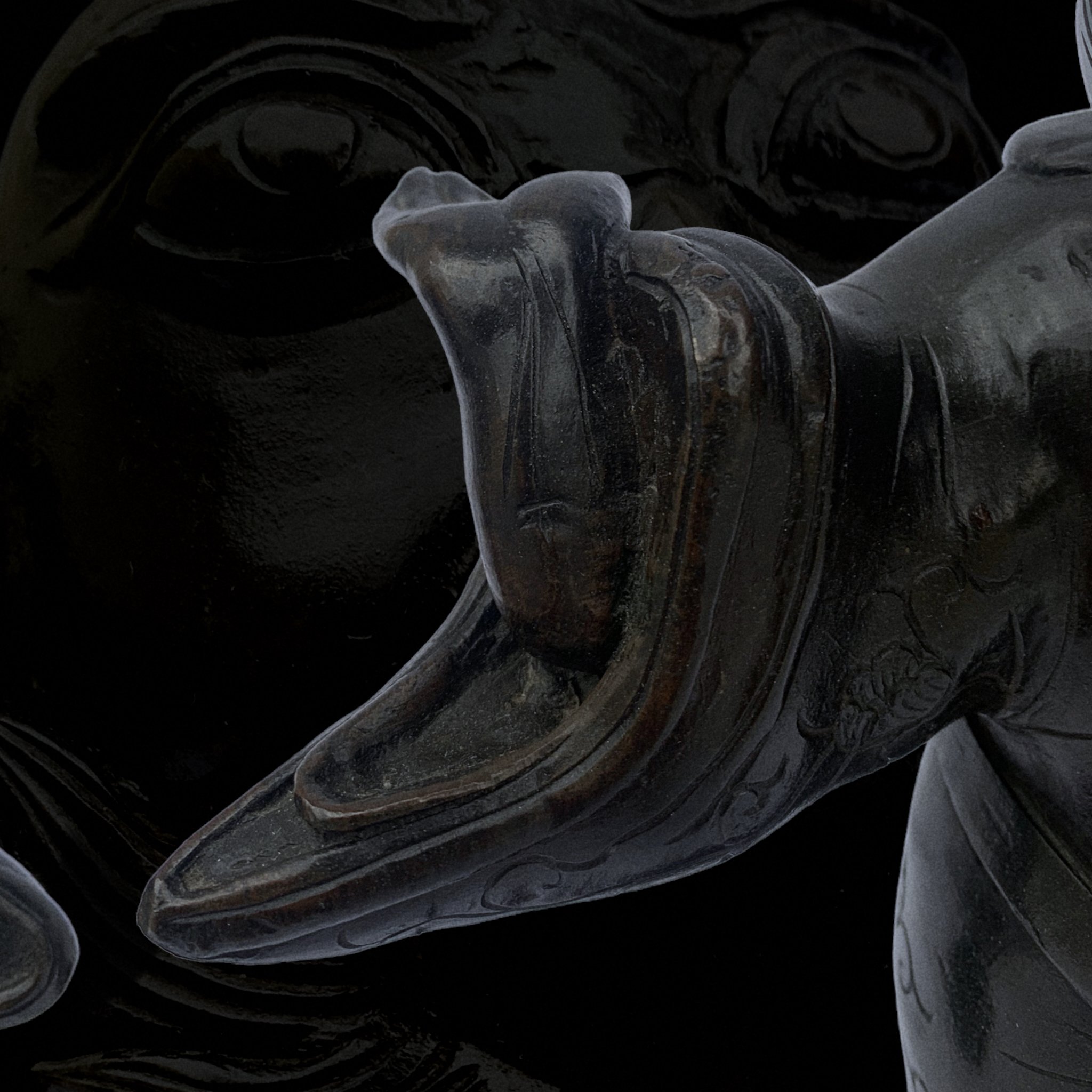 Close-up of a carved, dark-colored statue of a mythical creature with an open mouth, possibly a dragon or lion, with detailed facial features and textured surface.