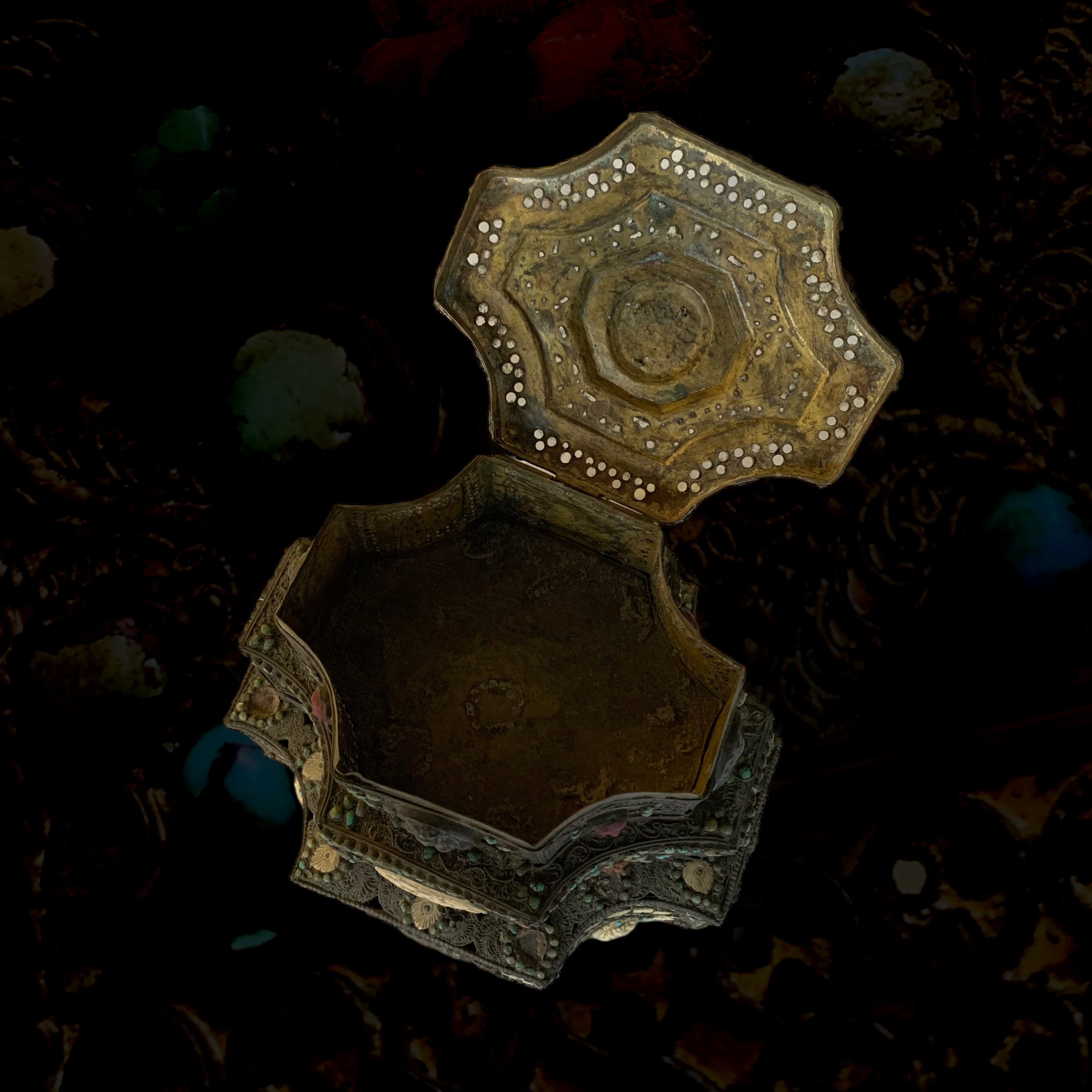 An ornate, metallic container with a flower-like shape, partially submerged in dark water with rocks and pebbles.
