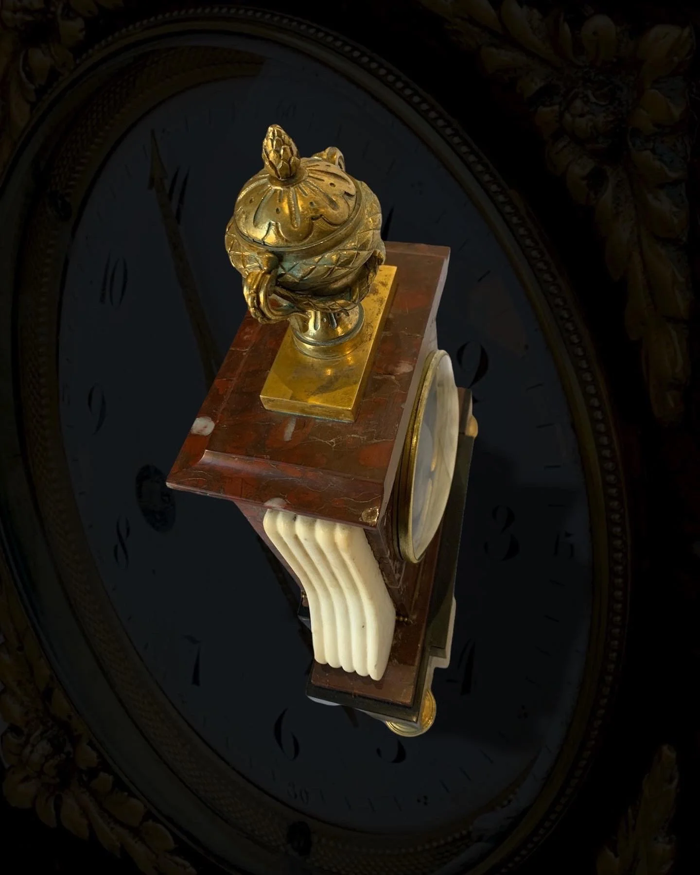 Close-up of an ornate, vintage clock with a gold decorative finial on top, mounted on a brown marble base with cream-colored details.