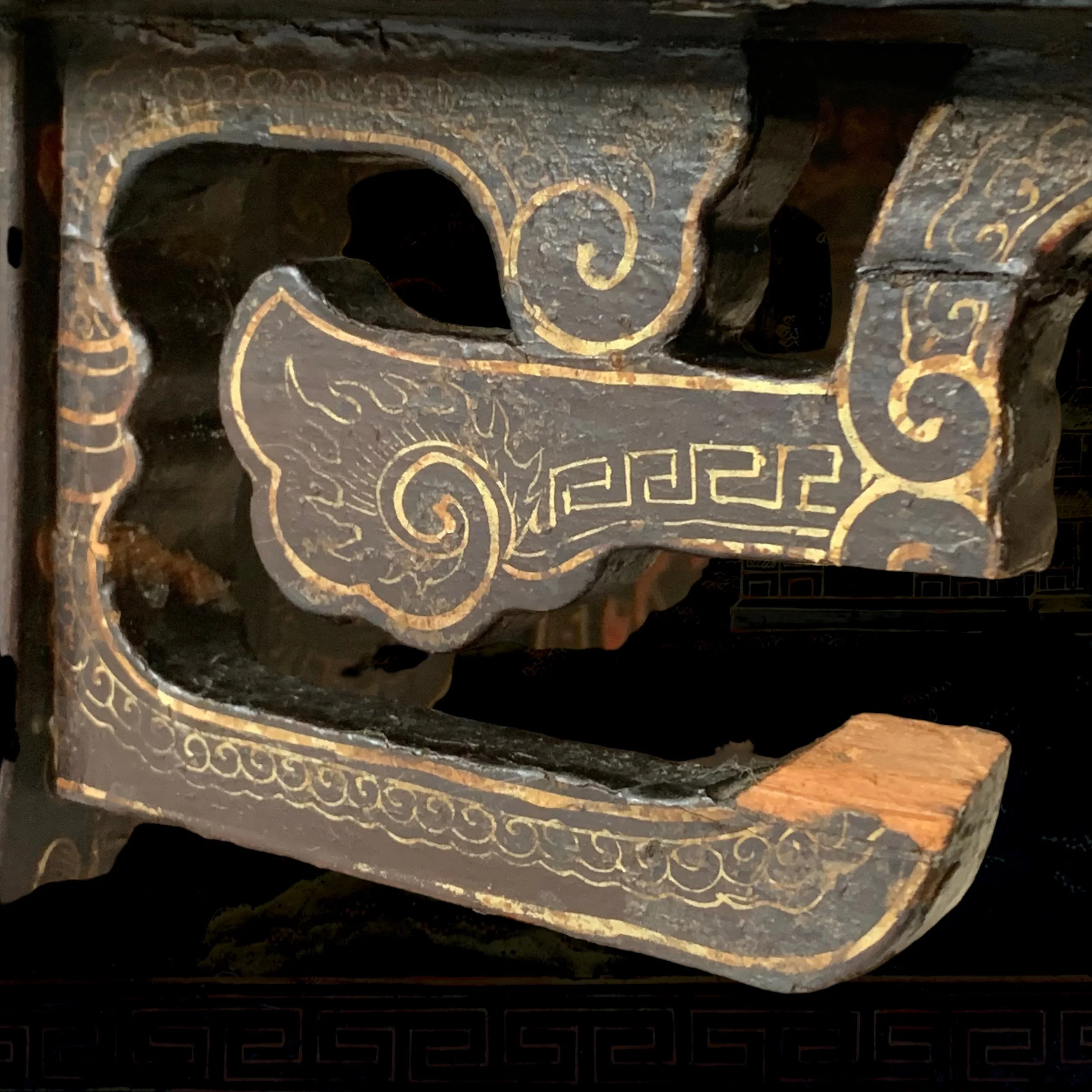 Close-up of an ornate, carved wooden piece with gold and black decorative patterns, possibly an antique furniture or architectural element.