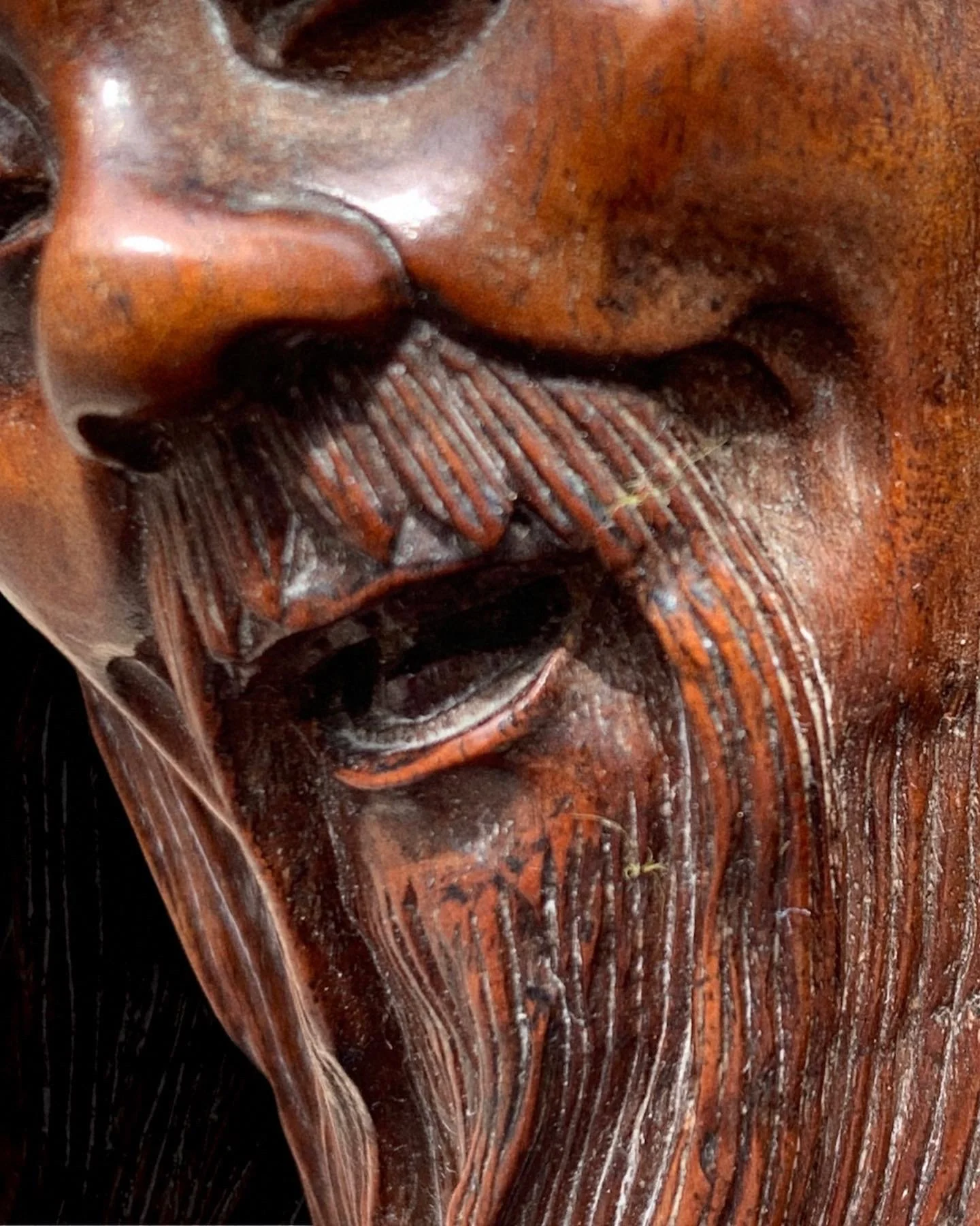 Close-up of a wooden carved sculpture of a face, showing detailed facial features and flowing hair.