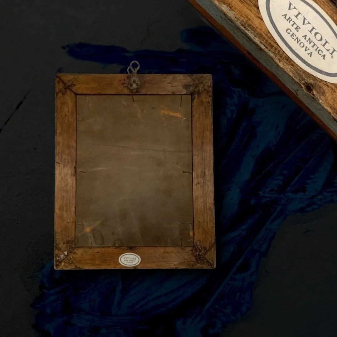 Flat wooden picture frame on a dark surface, with a blue cloth partially underneath and a carved wooden box with a label on the corner.