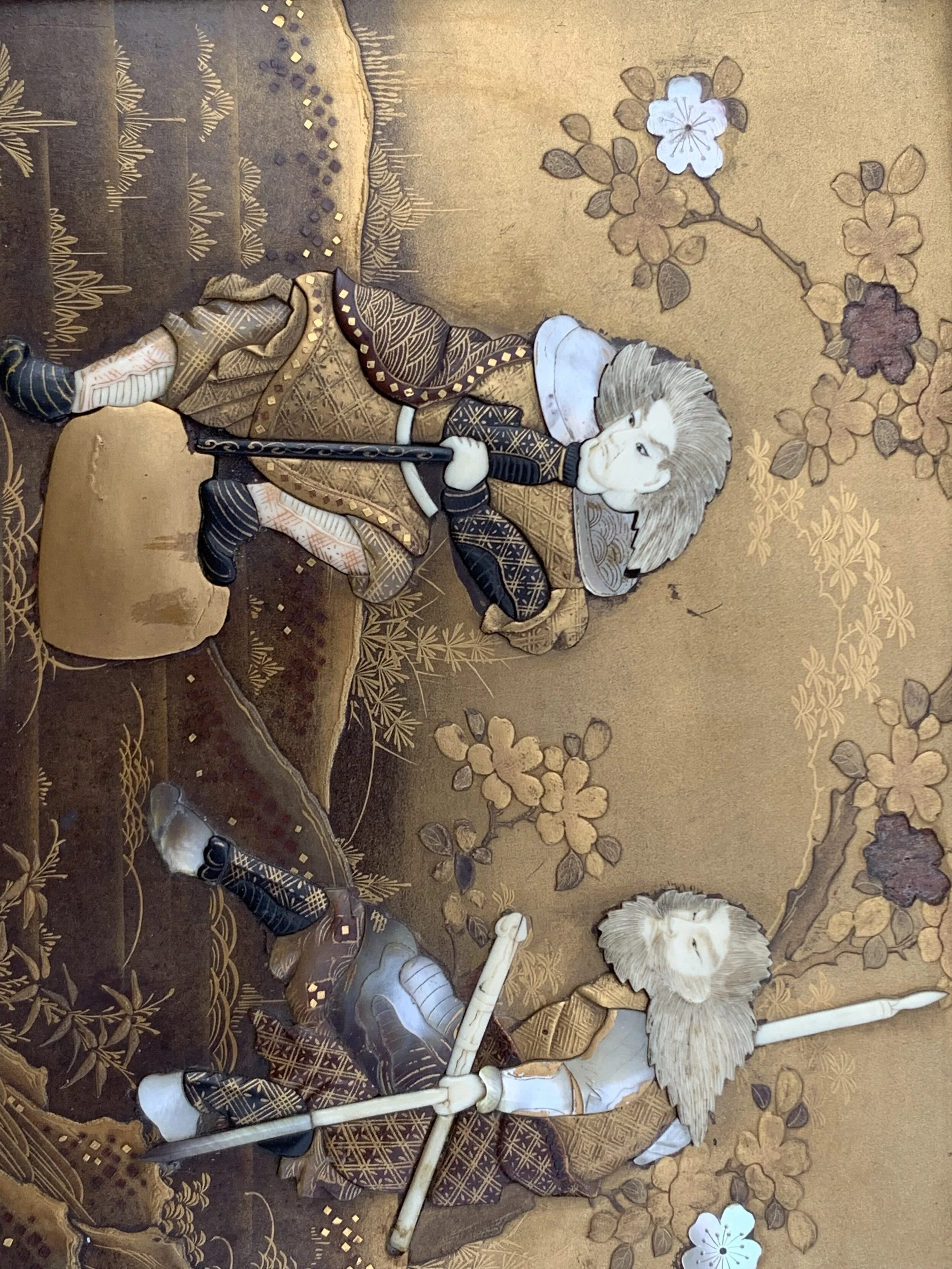 Traditional Japanese artwork featuring two figures with lions, dressed in elaborate clothing, holding spears, against a background of floral patterns and mountains.