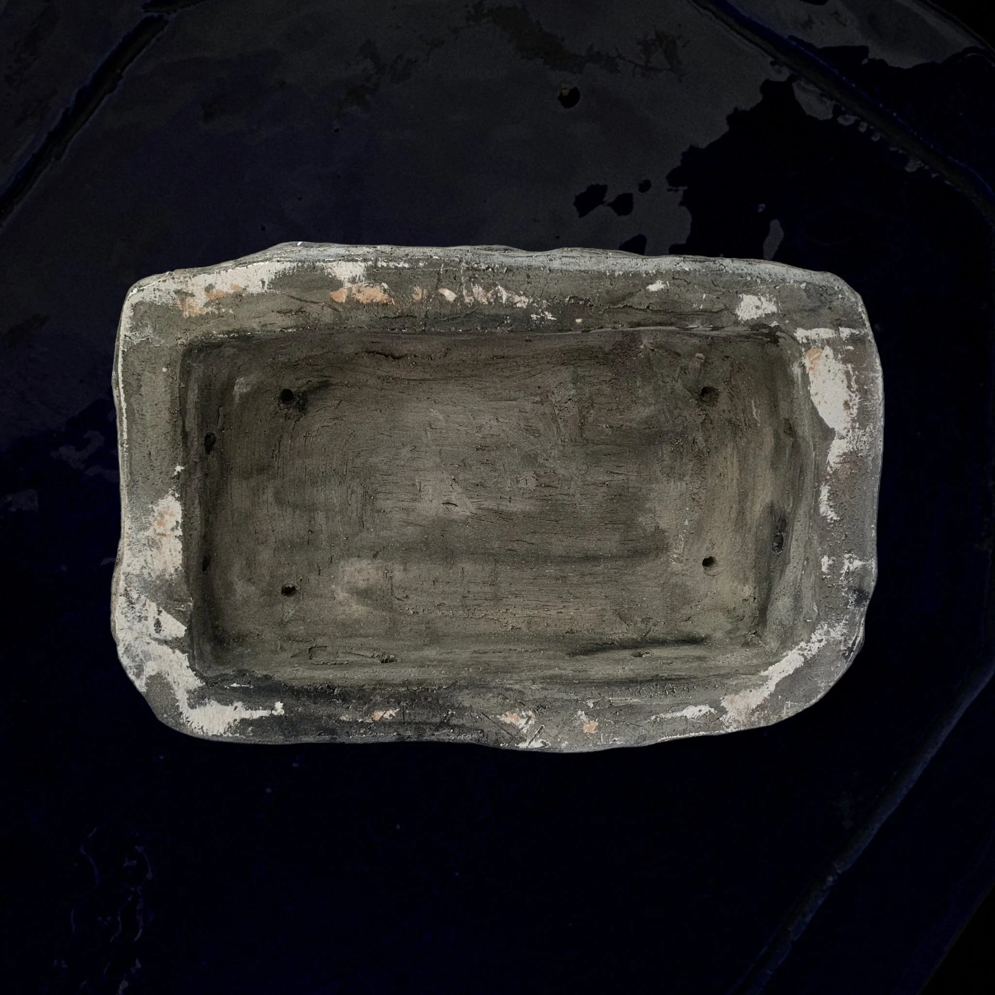 A weathered, rectangular stone planter with chipped edges, sitting on a dark surface.