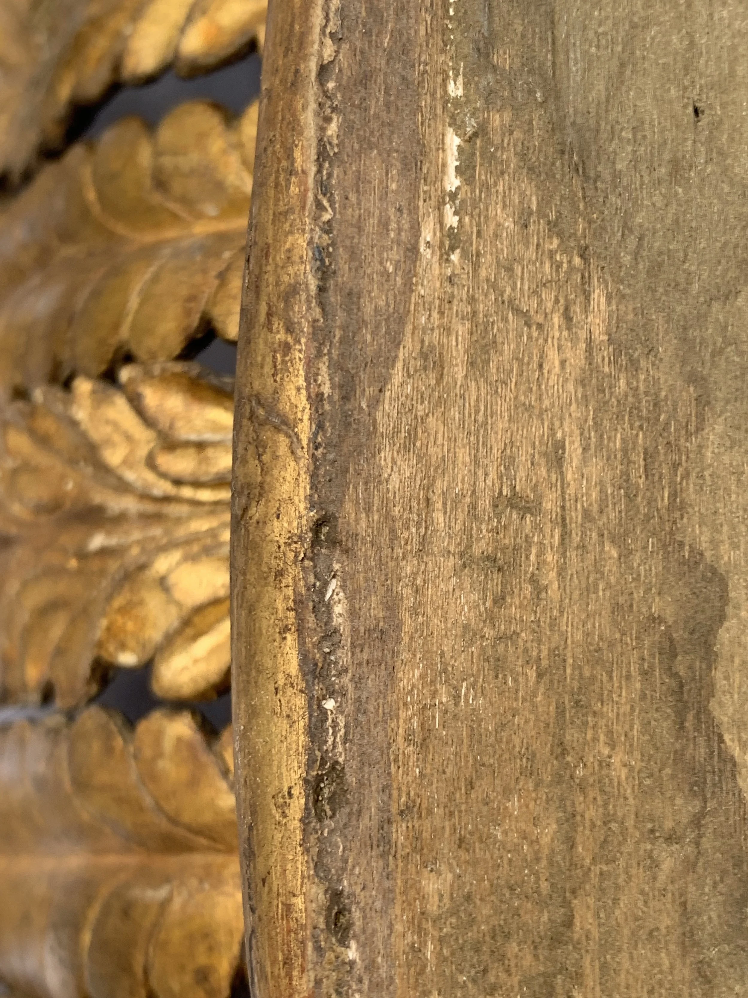 Close-up of a weathered wooden surface with carved decorative details in the background.