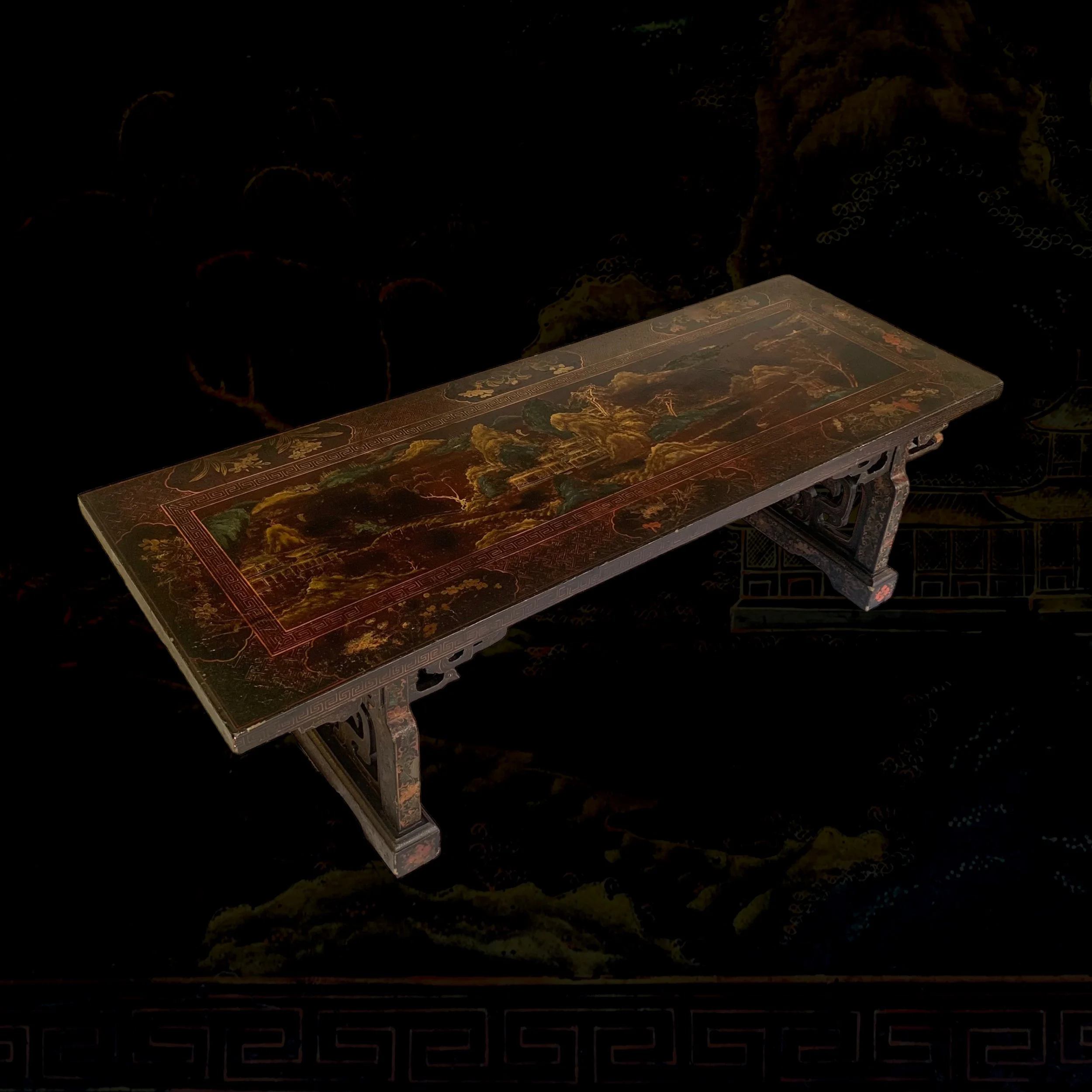 A rectangular Asian-style wooden table with intricate designs and landscape artwork, featuring mountains, trees, and water, on a dark background.