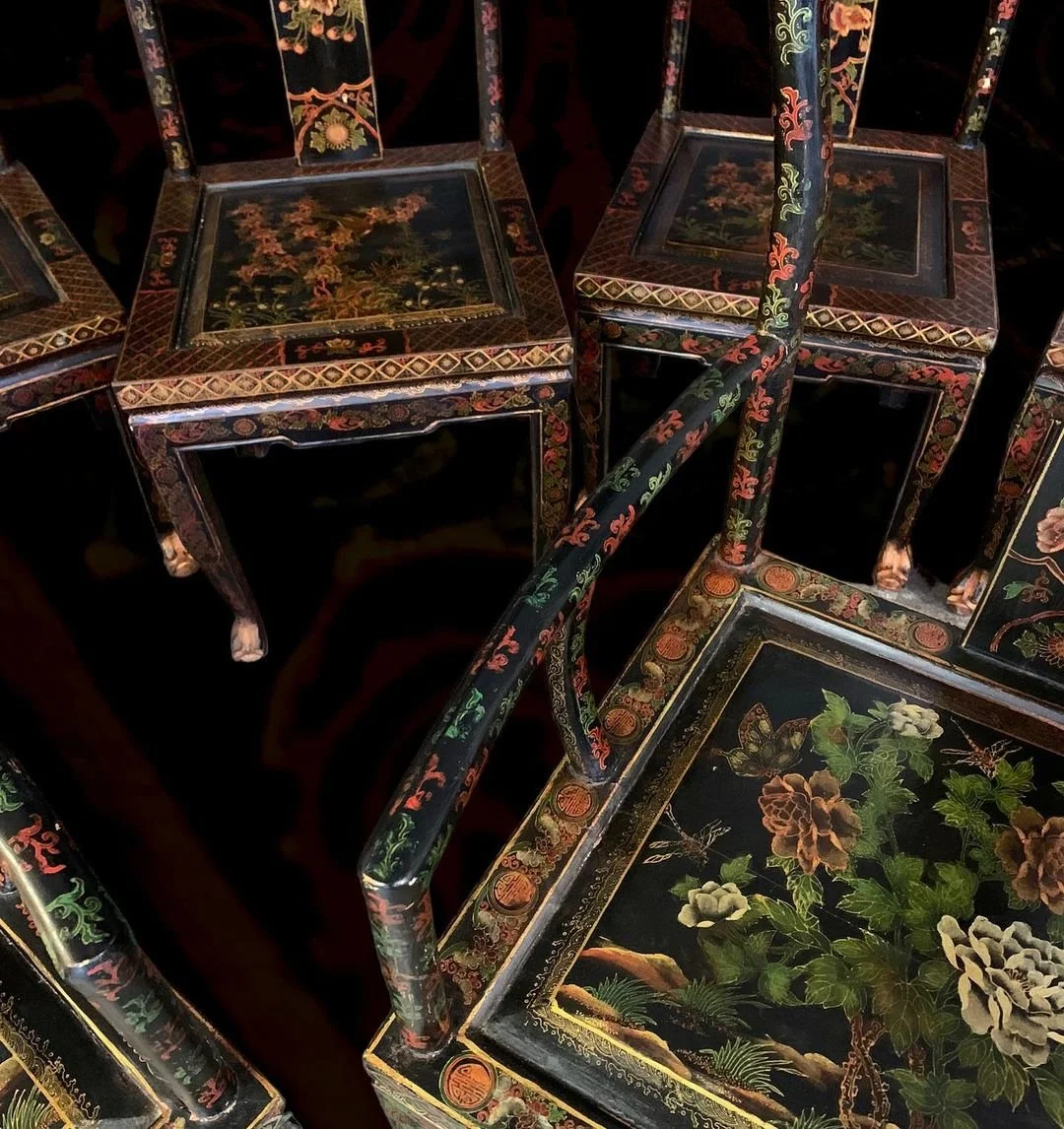 Close-up of black lacquered furniture with floral and nature-themed painted designs, including tables and chairs with intricate patterns.