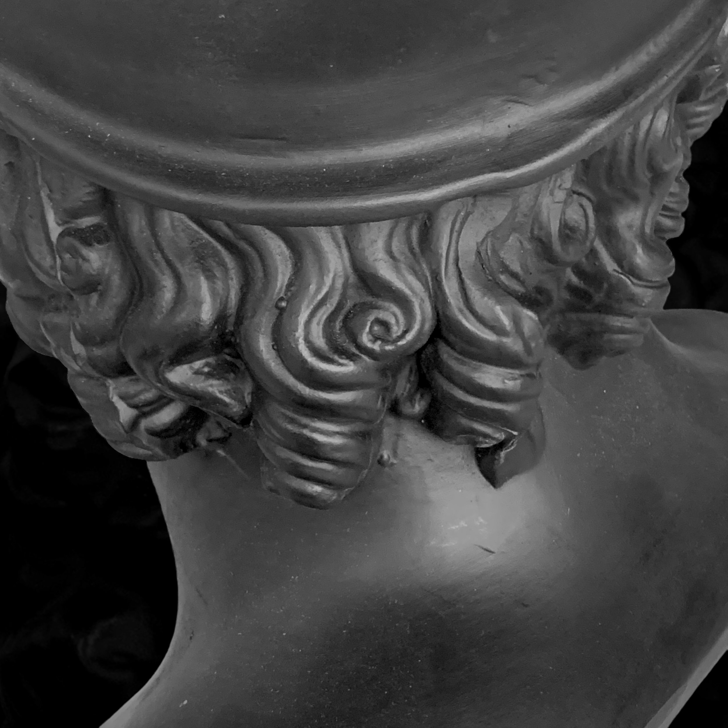 Close-up of a decorative sculpture featuring detailed, curly hair and a smooth face in black and white.