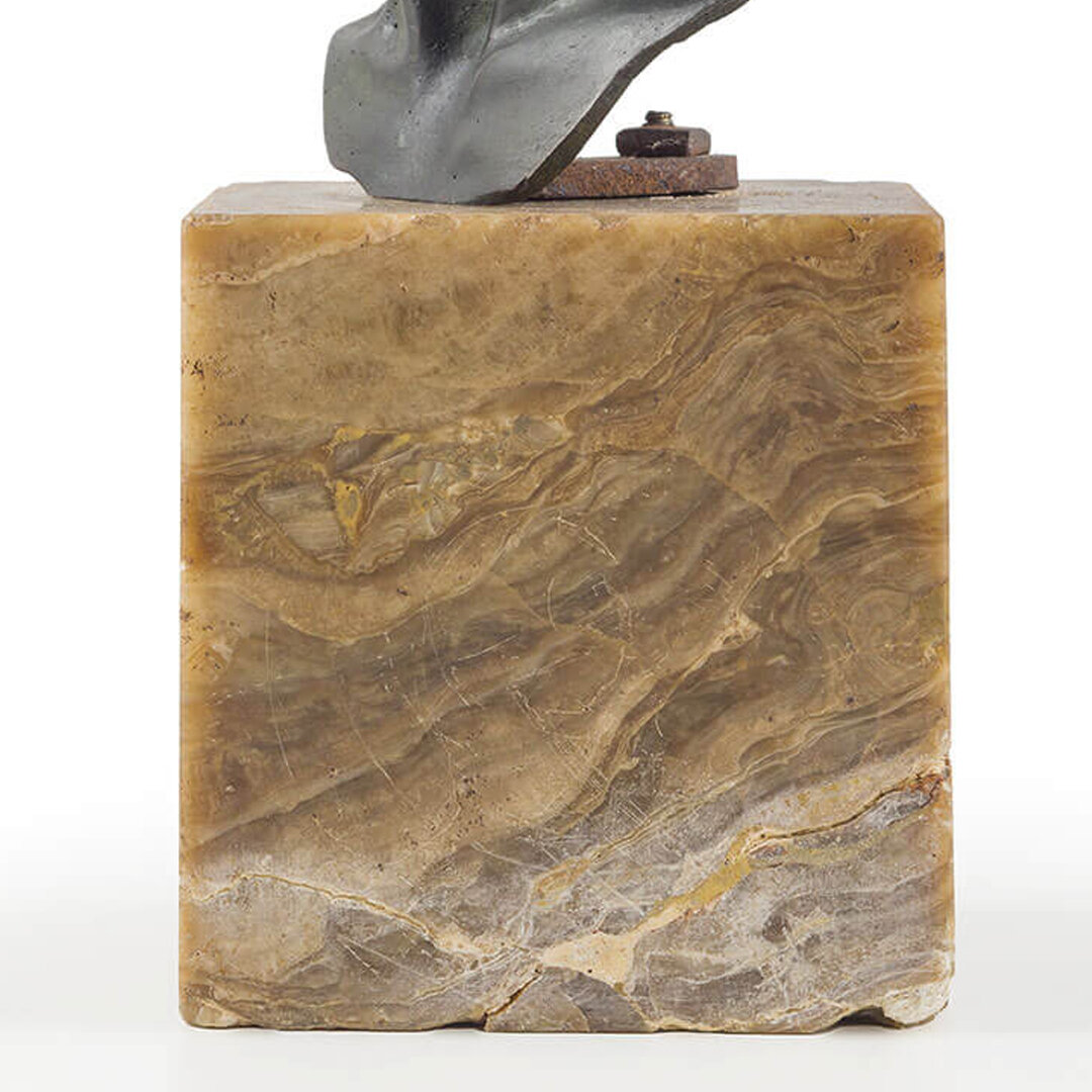 A sculpture featuring a metal hand and an abstract form mounted on a polished stone base.