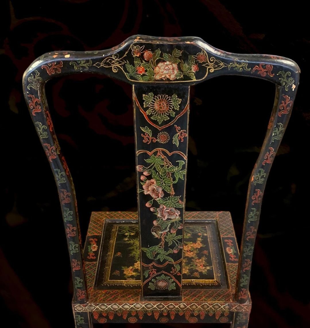 Decorative antique chair with black lacquer finish and colorful floral patterns in reds, greens, and gold. The chair has a high back, armrests, and a square seat, all adorned with intricate painted designs.