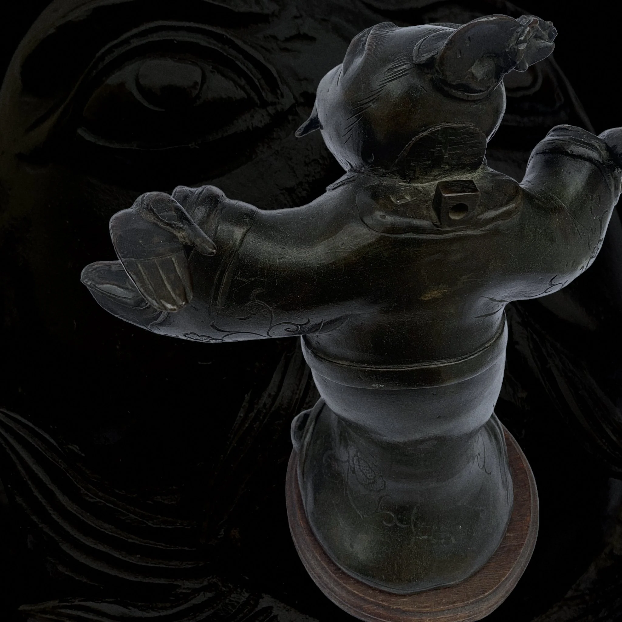 A carved dark wooden statue of a flamingo with one leg raised, standing on a circular base, reflected on a shiny black surface.