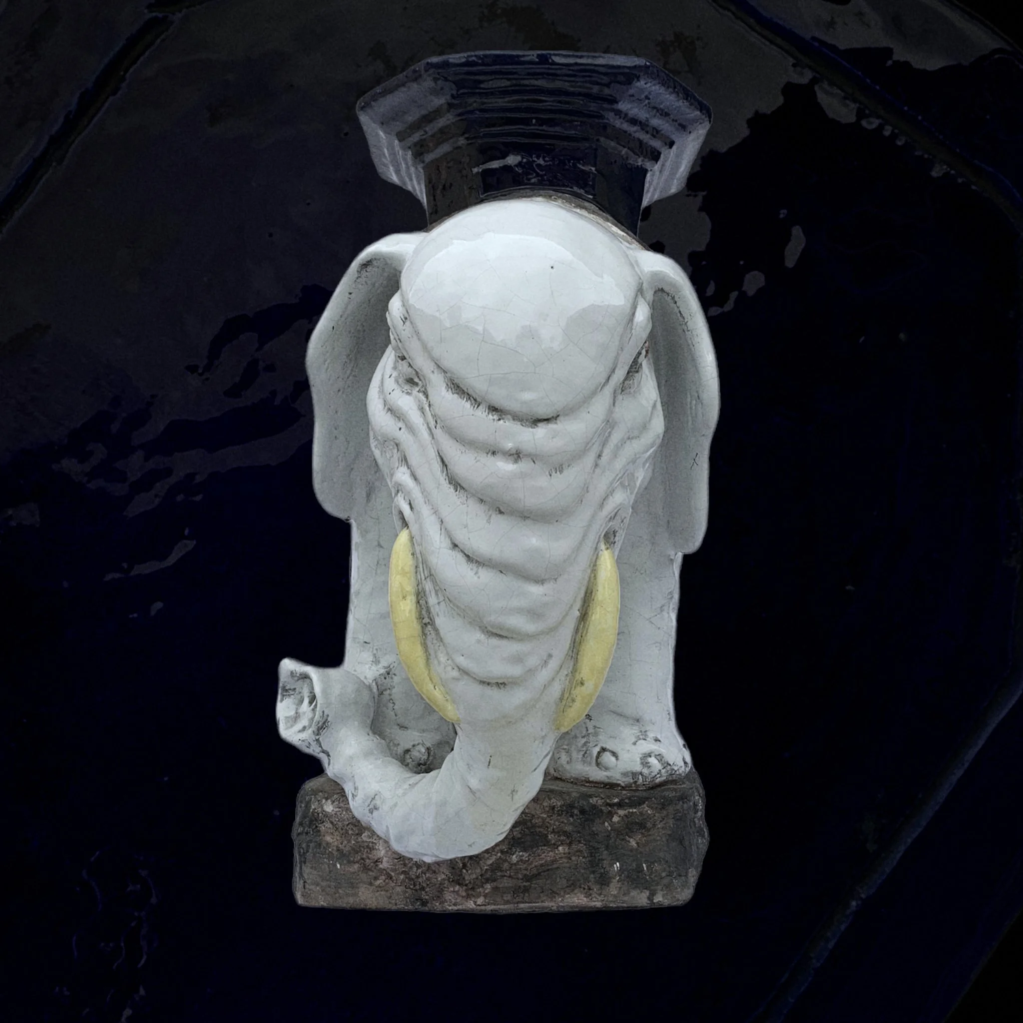 White elephant statue with yellow tusks, viewed from above on a dark surface.