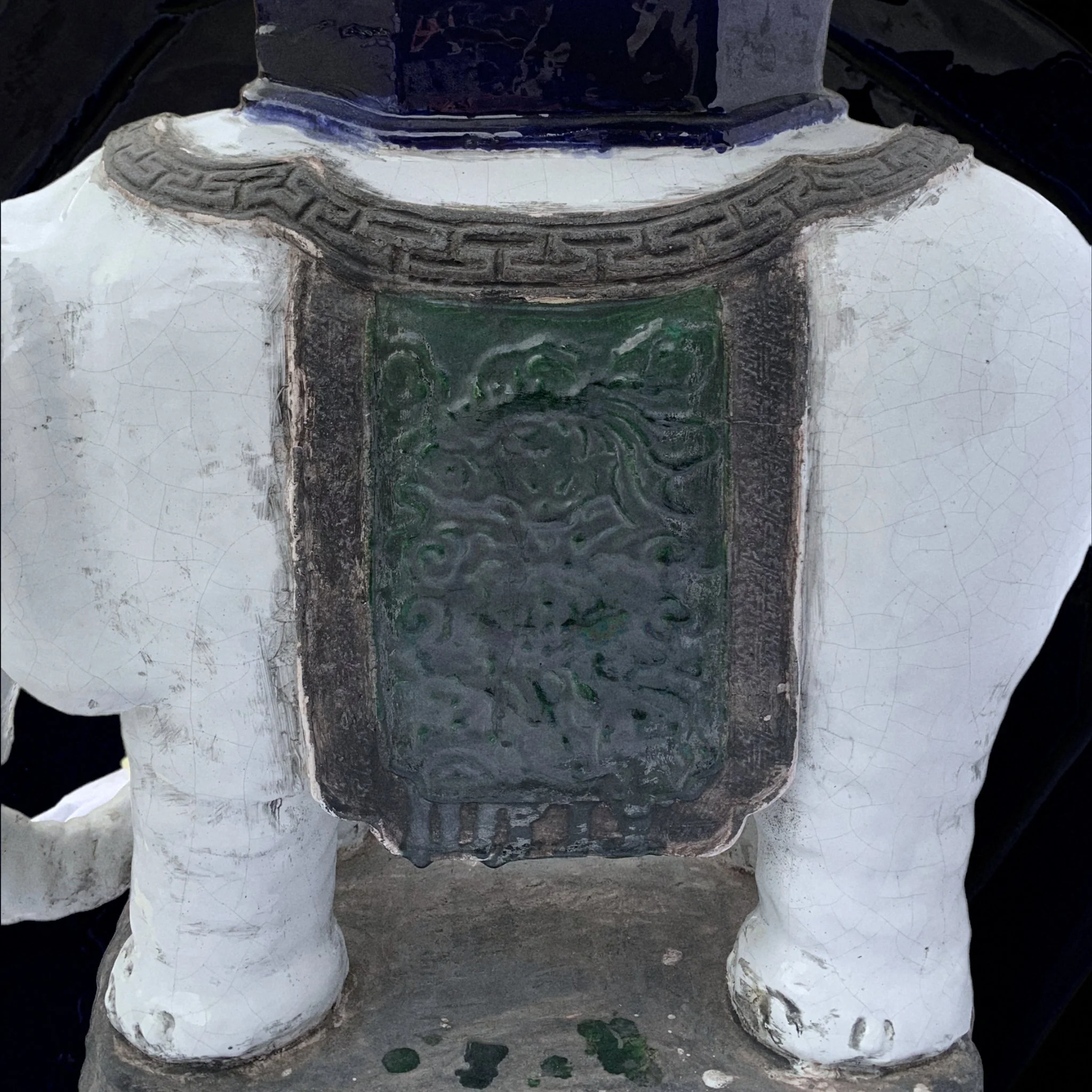Close-up of a ceramic statue of an elephant with a decorative plaque on its side, showing signs of wear and crackle glaze.