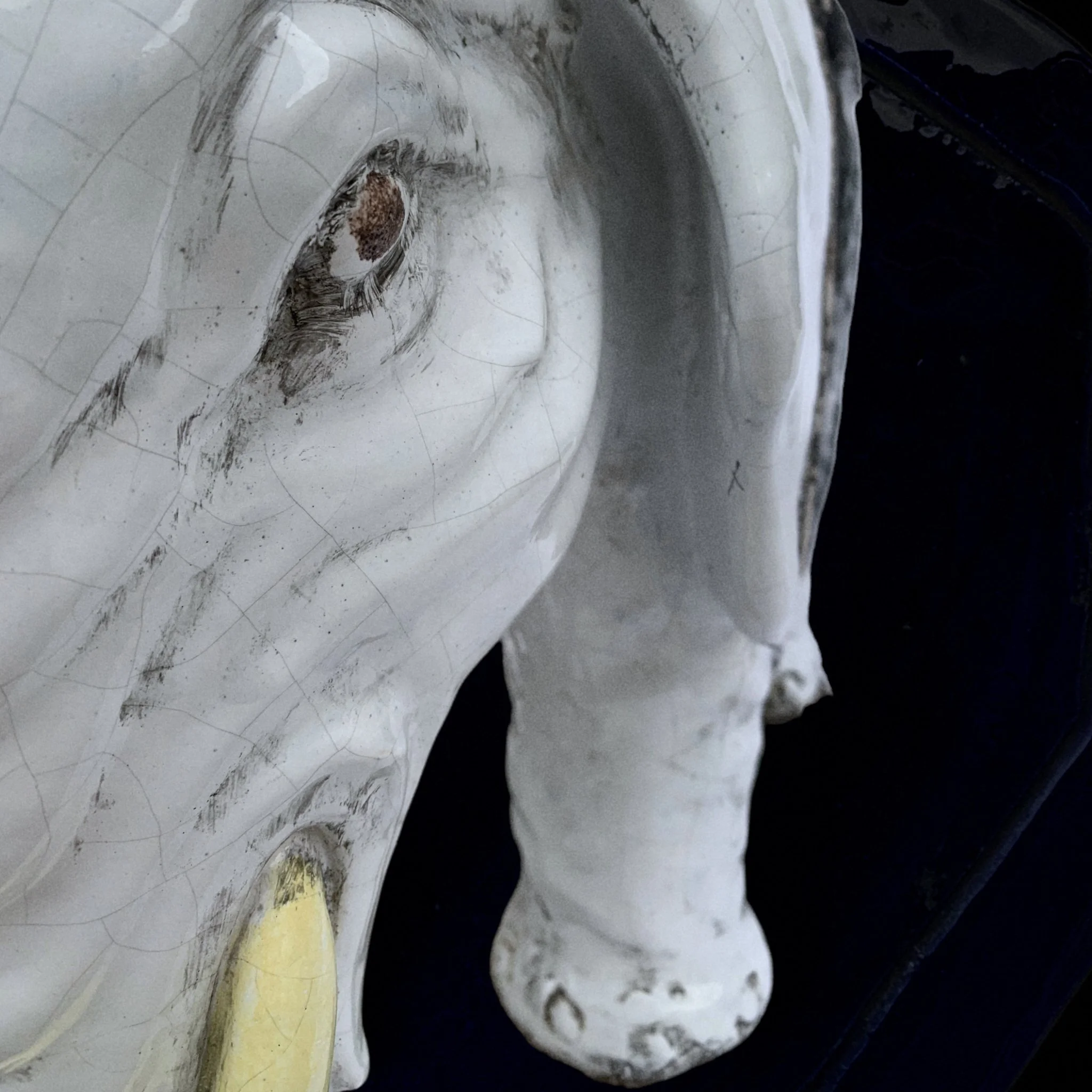 Close-up of a white ceramic or porcelain sculpture of a human face, possibly an angel, with detailed features including an eye, nose, and lips, and a golden detail near the chin.