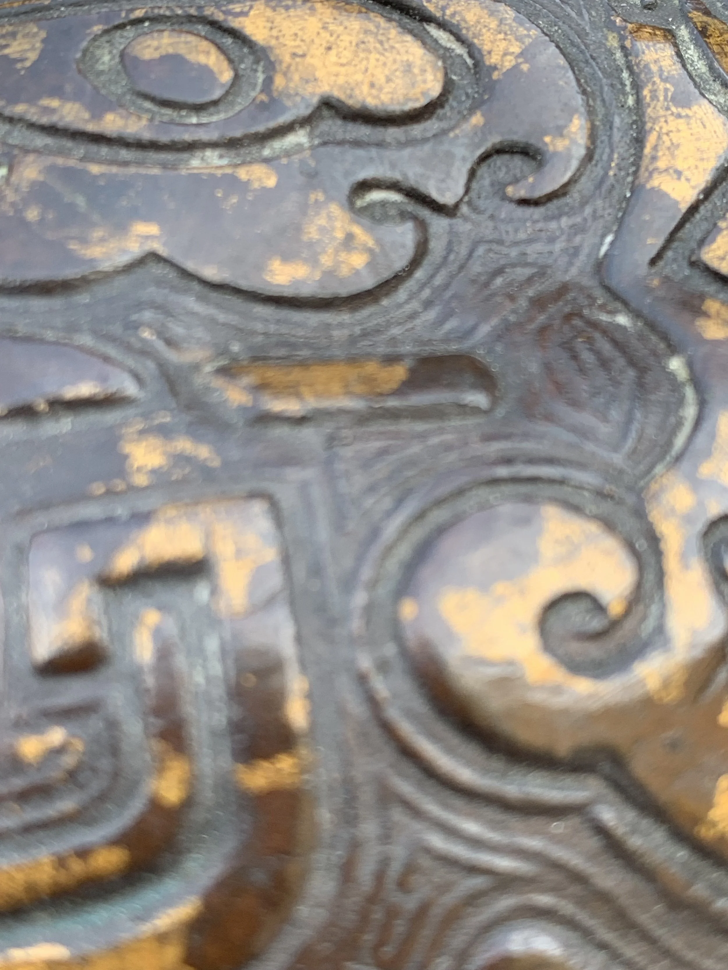 A close-up image of a metallic surface with embossed decorative patterns featuring swirls and geometric shapes.