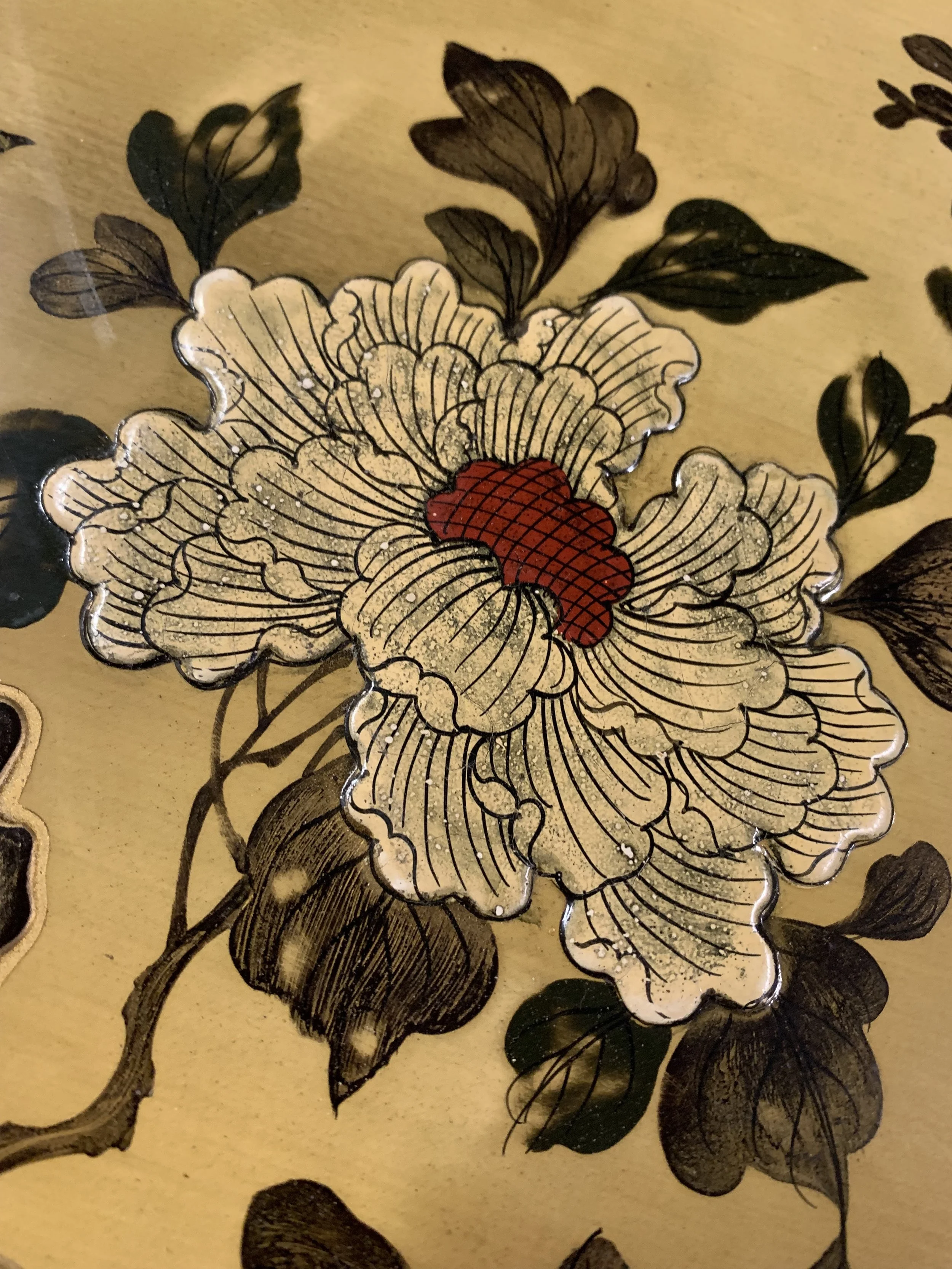 A detailed illustration of a peony flower with cream-colored petals, red center, and dark green leaves on a gold background.