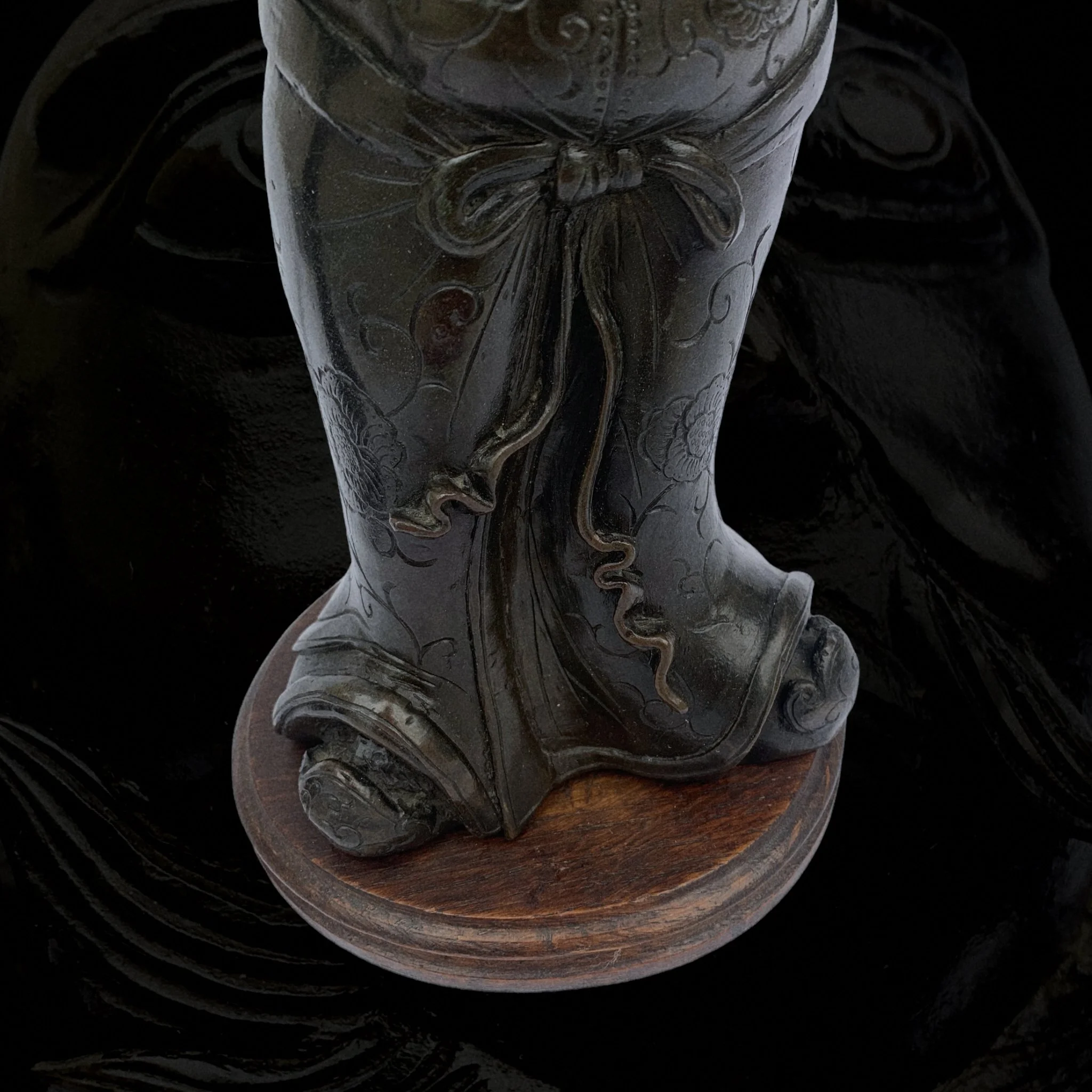 Close-up of a dark, carved sculpture of two faces kissing, mounted on a round wooden base.