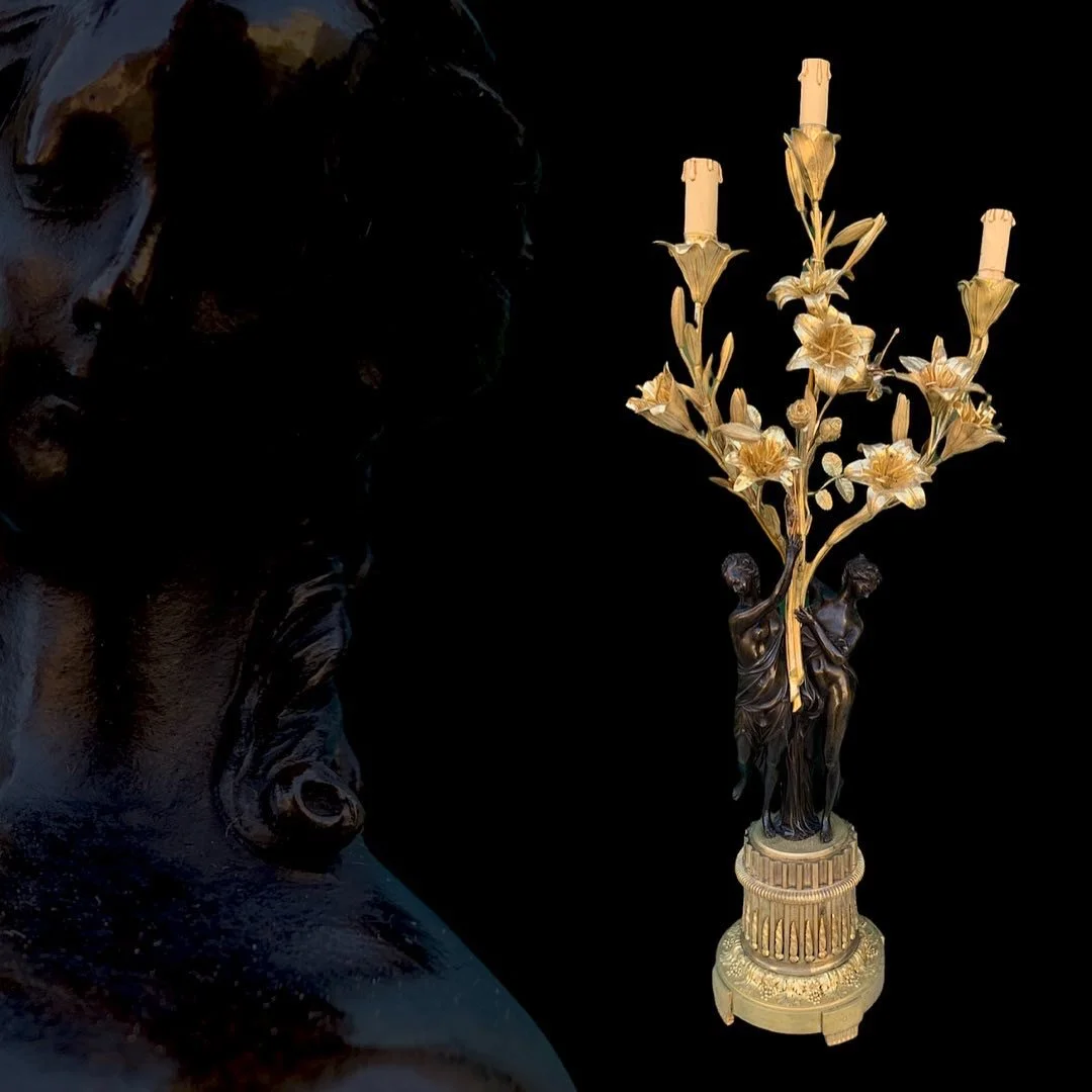 A black bronze sculpture of a woman's face beside an ornate gold-colored candelabrum with three candles and floral detailing.
