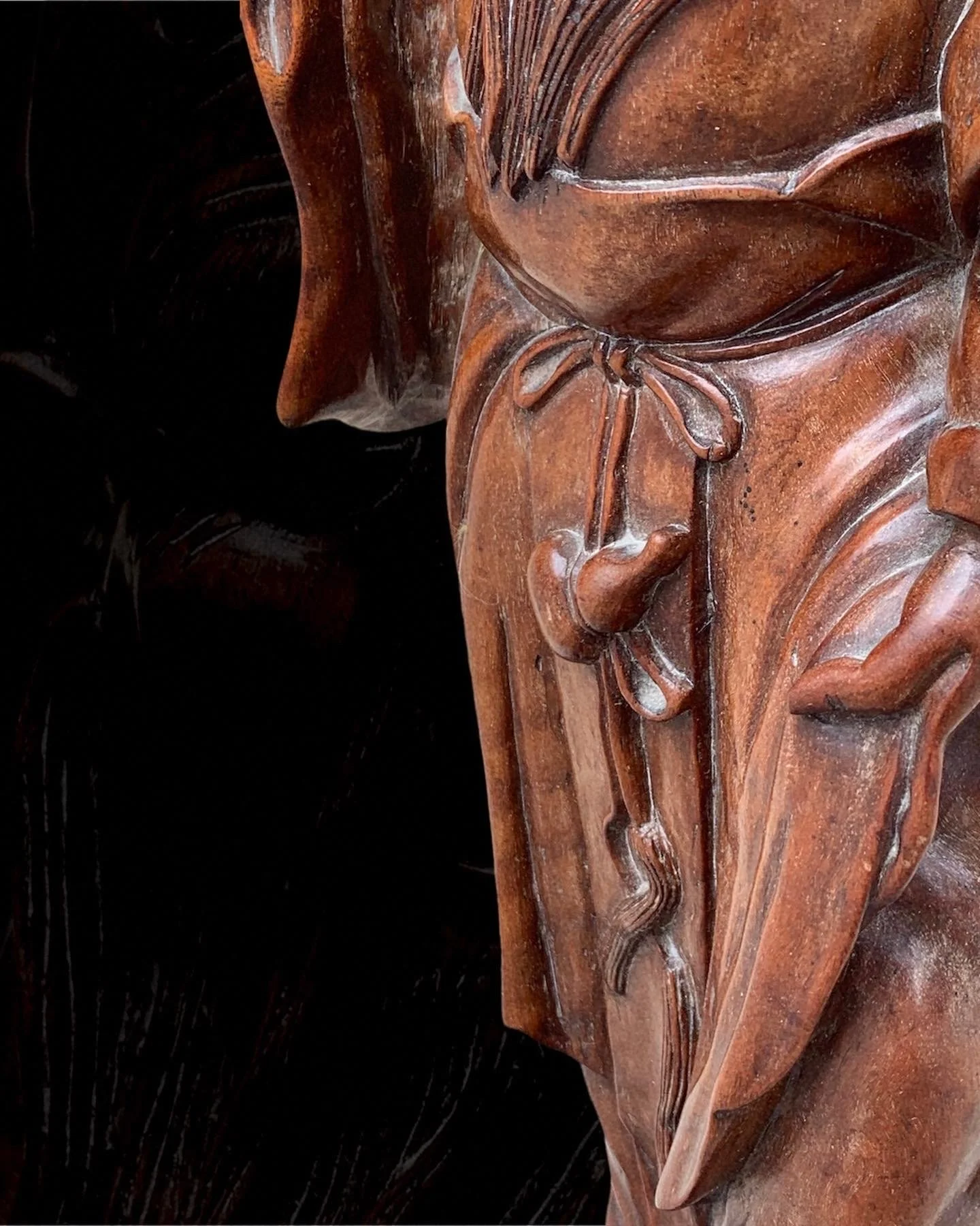 Close-up of a wooden sculpture of a person's face with long hair, a nose ring, earrings, and a tied shirt.