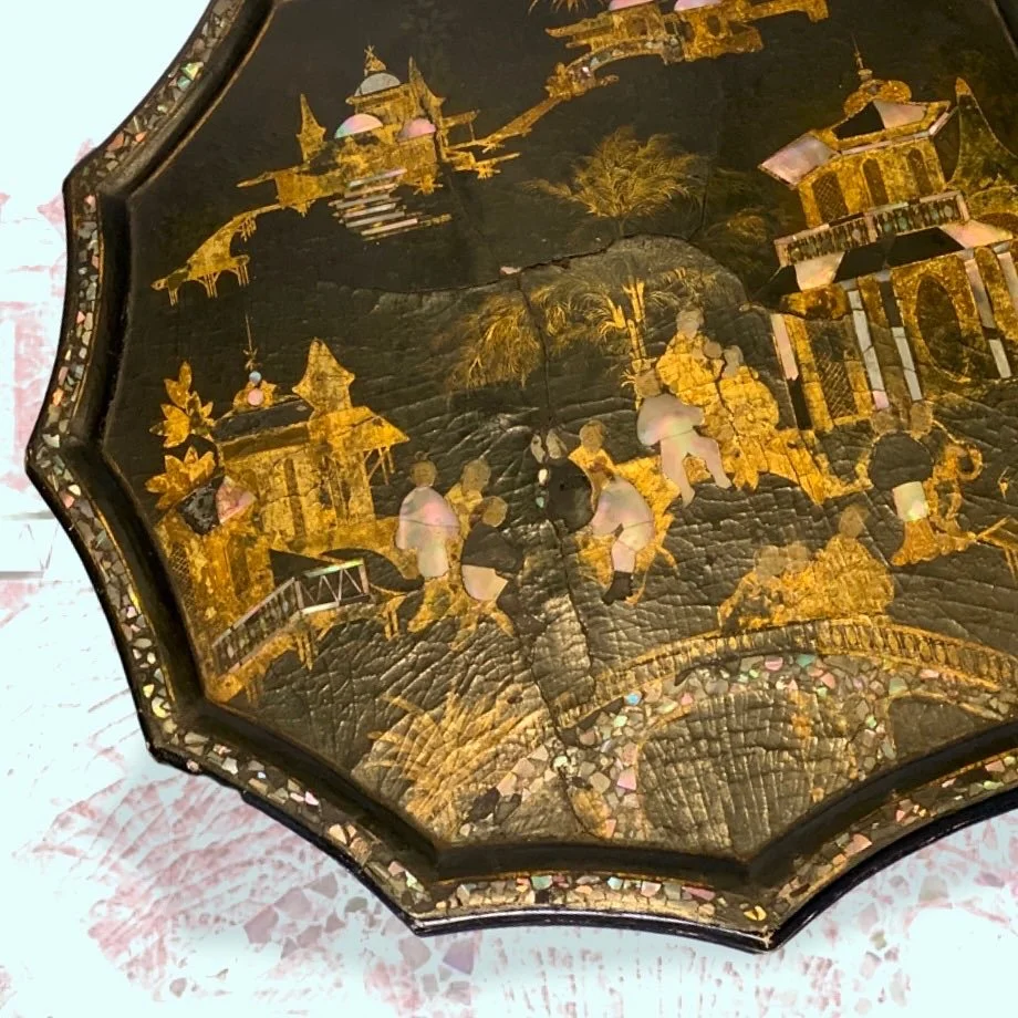 An octagonal decorative box with a detailed scene in gold and pastel colors, depicting people, buildings, and nature, on a black background.