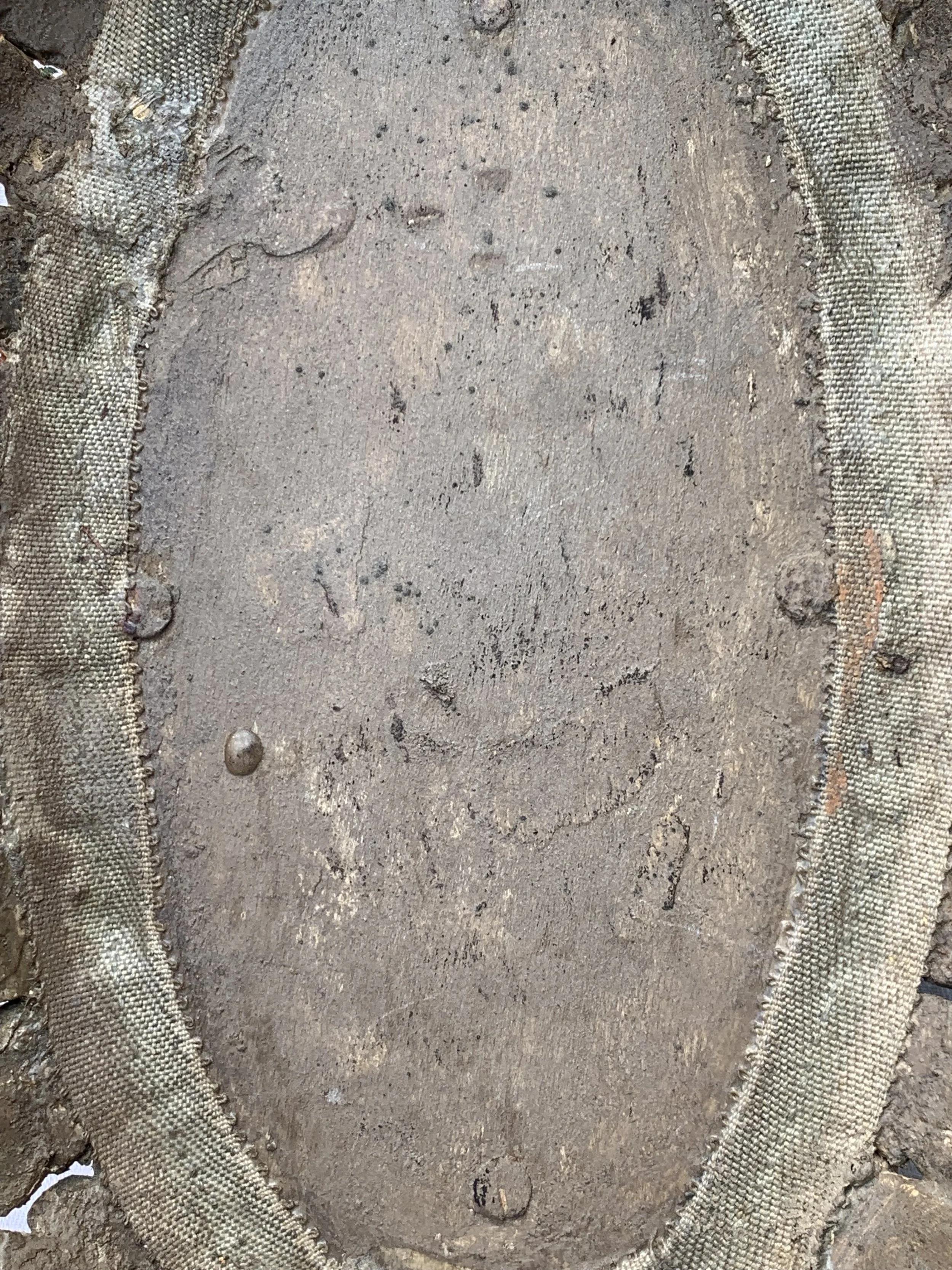 Close-up of a worn, oval-shaped military badge with faded markings and a fabric border, partially covered in dirt.