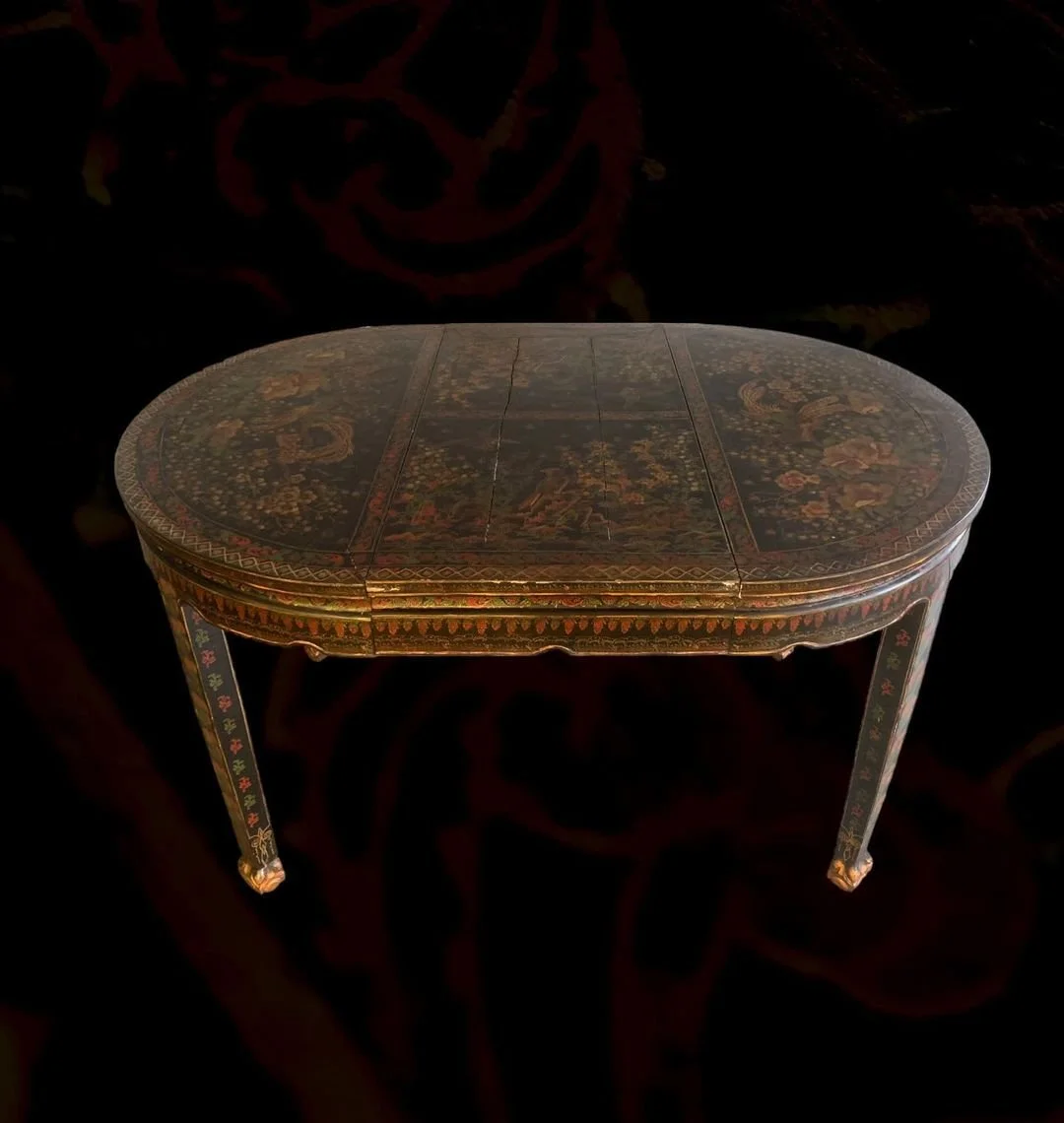 An ornate, oval-shaped wooden table with floral and nature-themed decorative patterns, including birds and flowers, on its surface and legs.