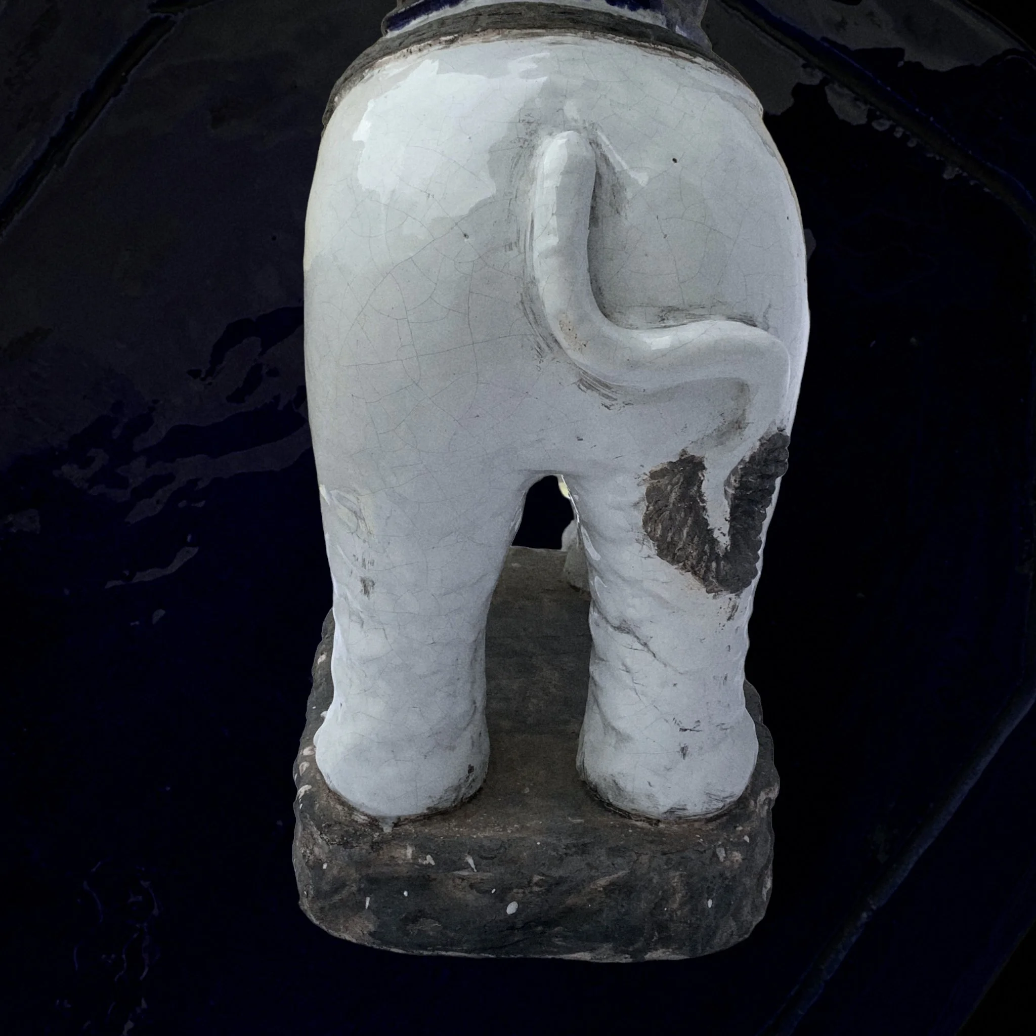 A ceramic elephant figurine facing away, painted white with black accents, standing on a stone base.