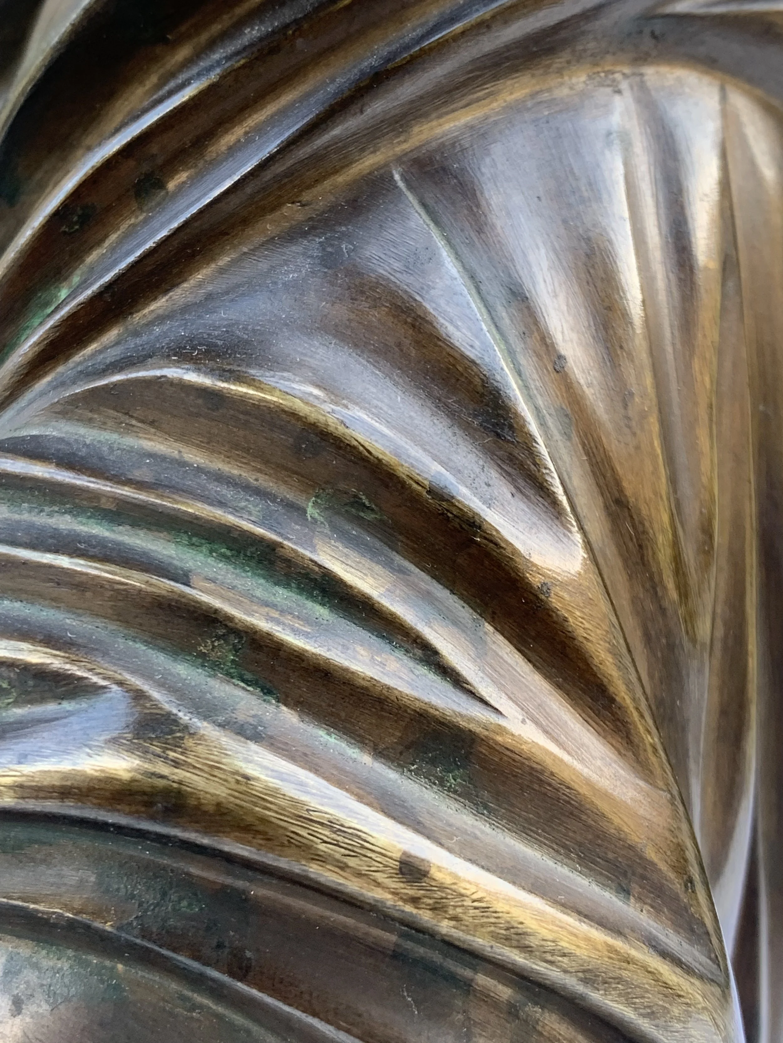 Close-up of a decorative, carved, and polished metallic surface with curved, flowing lines and a shiny finish.
