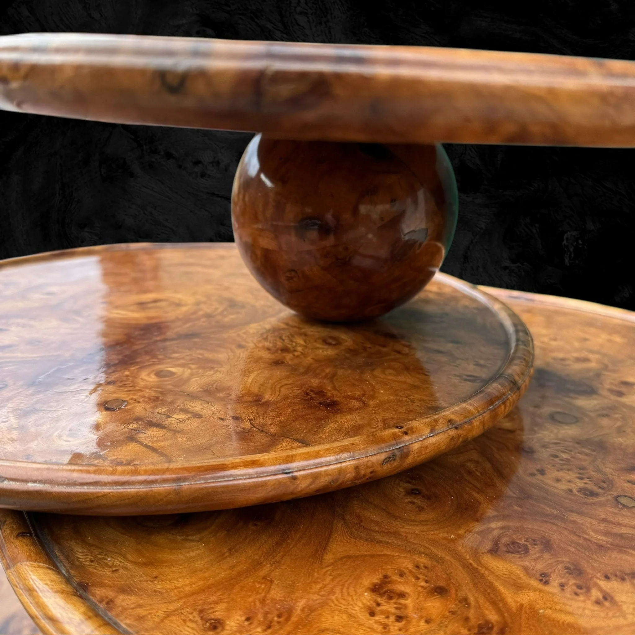 Close-up of a polished wooden table with a spherical wooden object resting on a small round wooden platform, showcasing the wood grain and glossy finish.