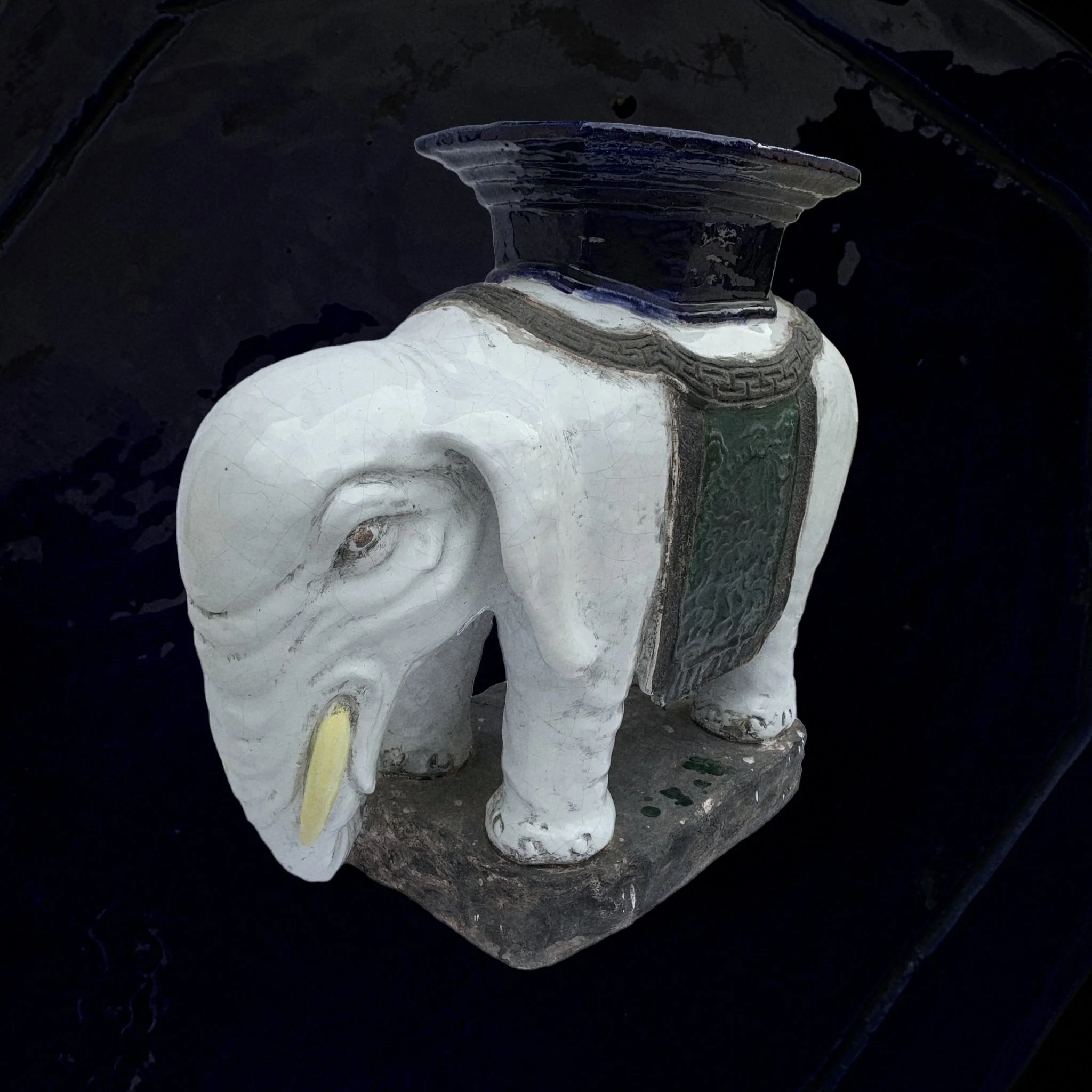 A decorative ceramic sculpture of an elephant with a saddle and a jar on its back.