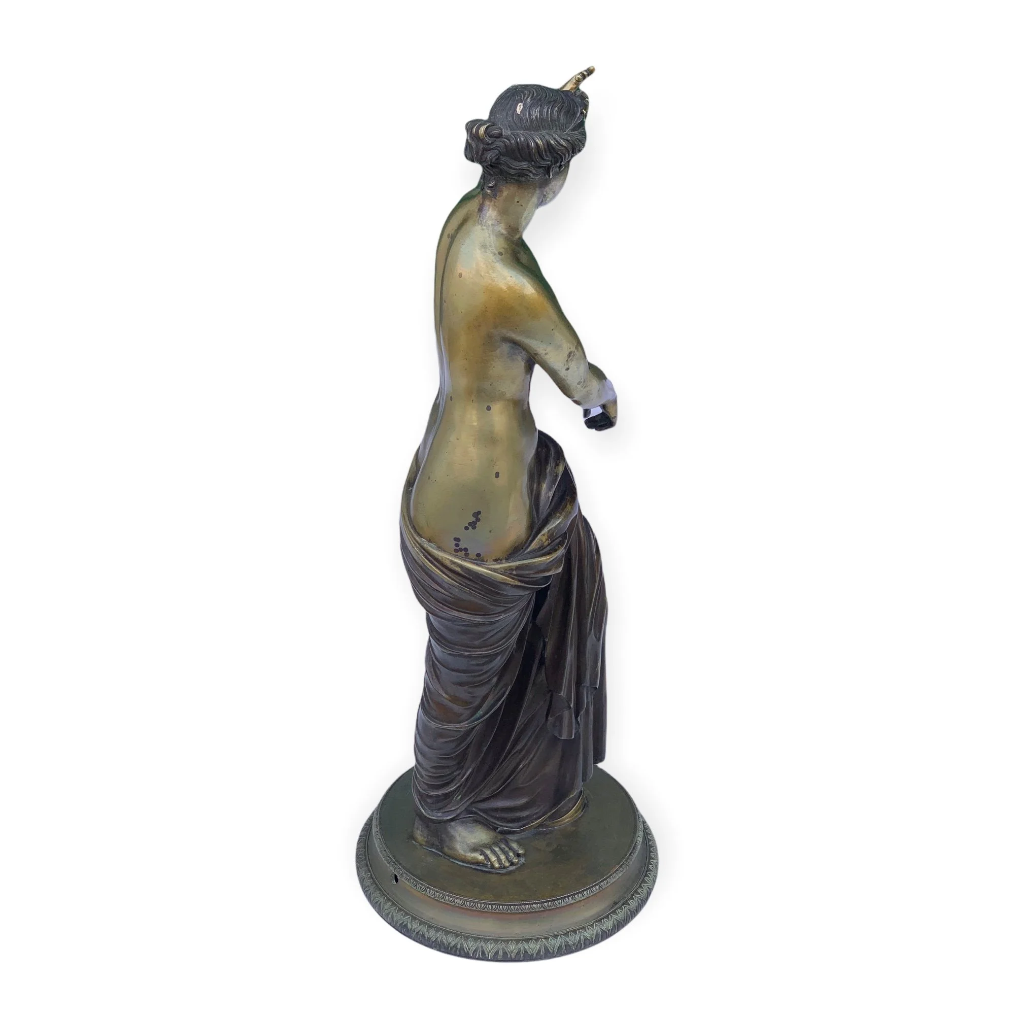 A bronze sculpture of a woman with her back turned, wearing a flowing garment draped over her hips, standing on a round base.