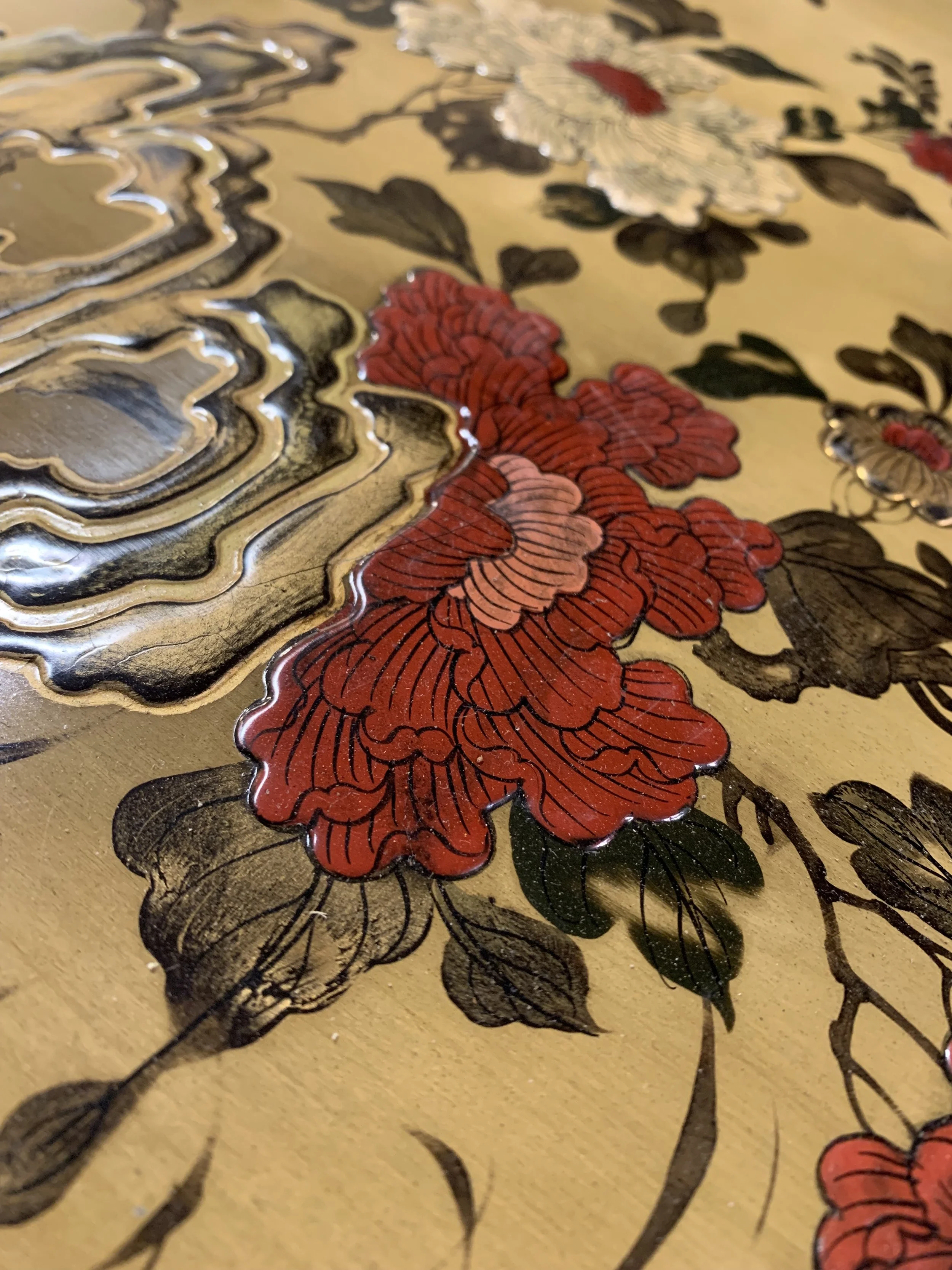 Close-up view of a decorative metallic surface with embossed red and black floral patterns.