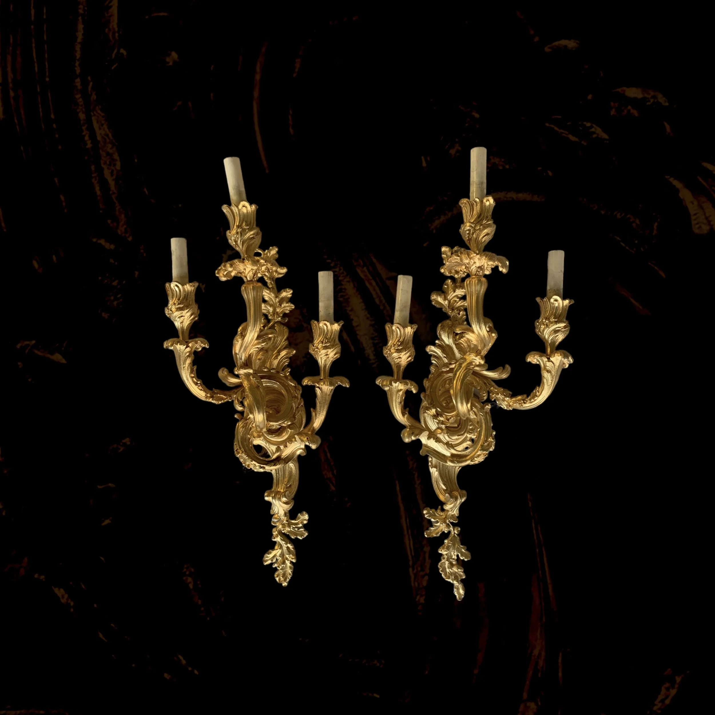 Ornate gold wall sconces with candle-like lights against a dark background.