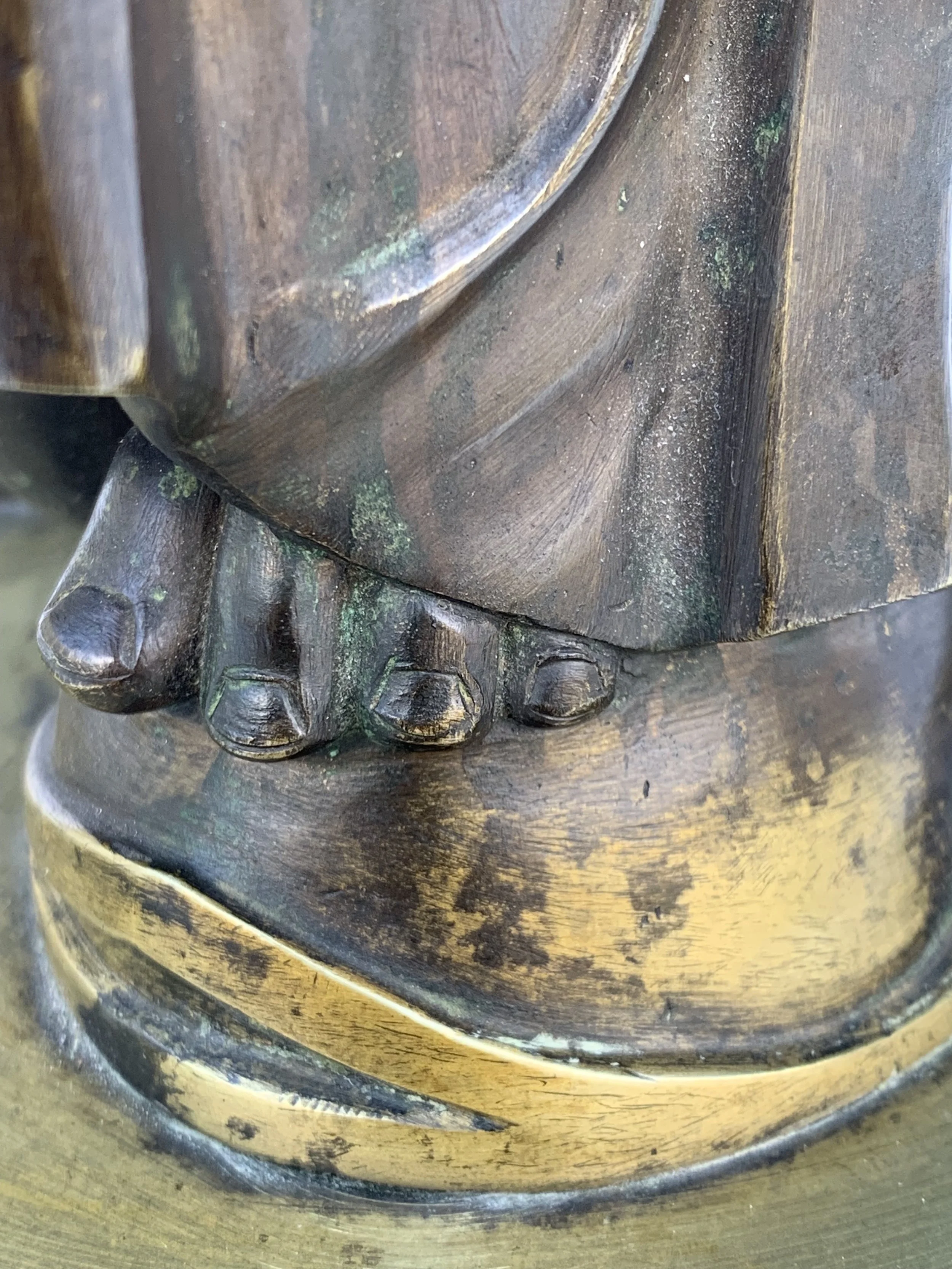 Close-up of a brass or bronze statue's feet, showing detailed toes and the base, with some green patina and wear.