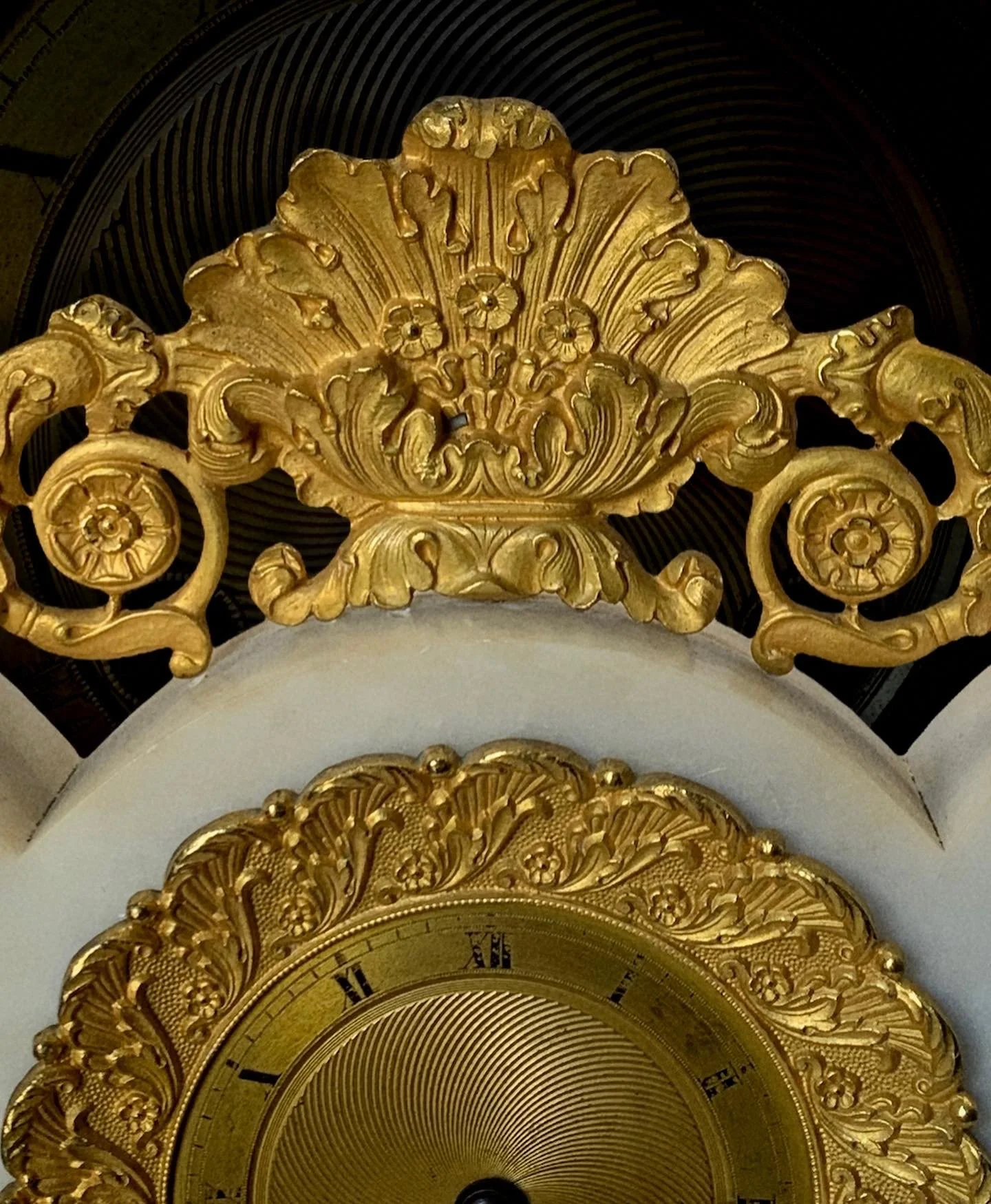 Close-up of an ornate gold decorative crest and clock face with Roman numerals.