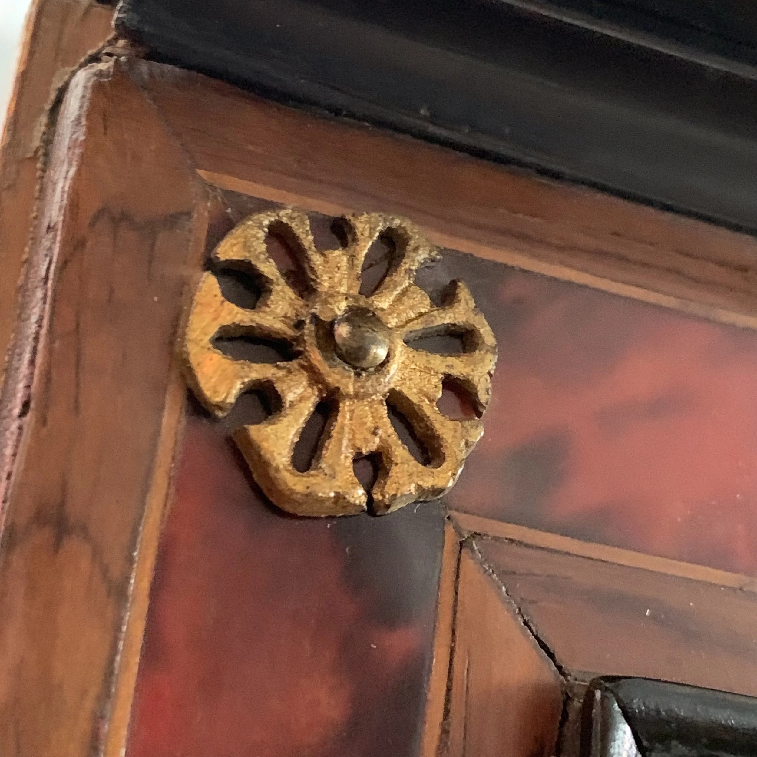 Close-up of a decorative, vintage brass drawer or cabinet knob with a floral or wheel design, attached to a wooden surface.