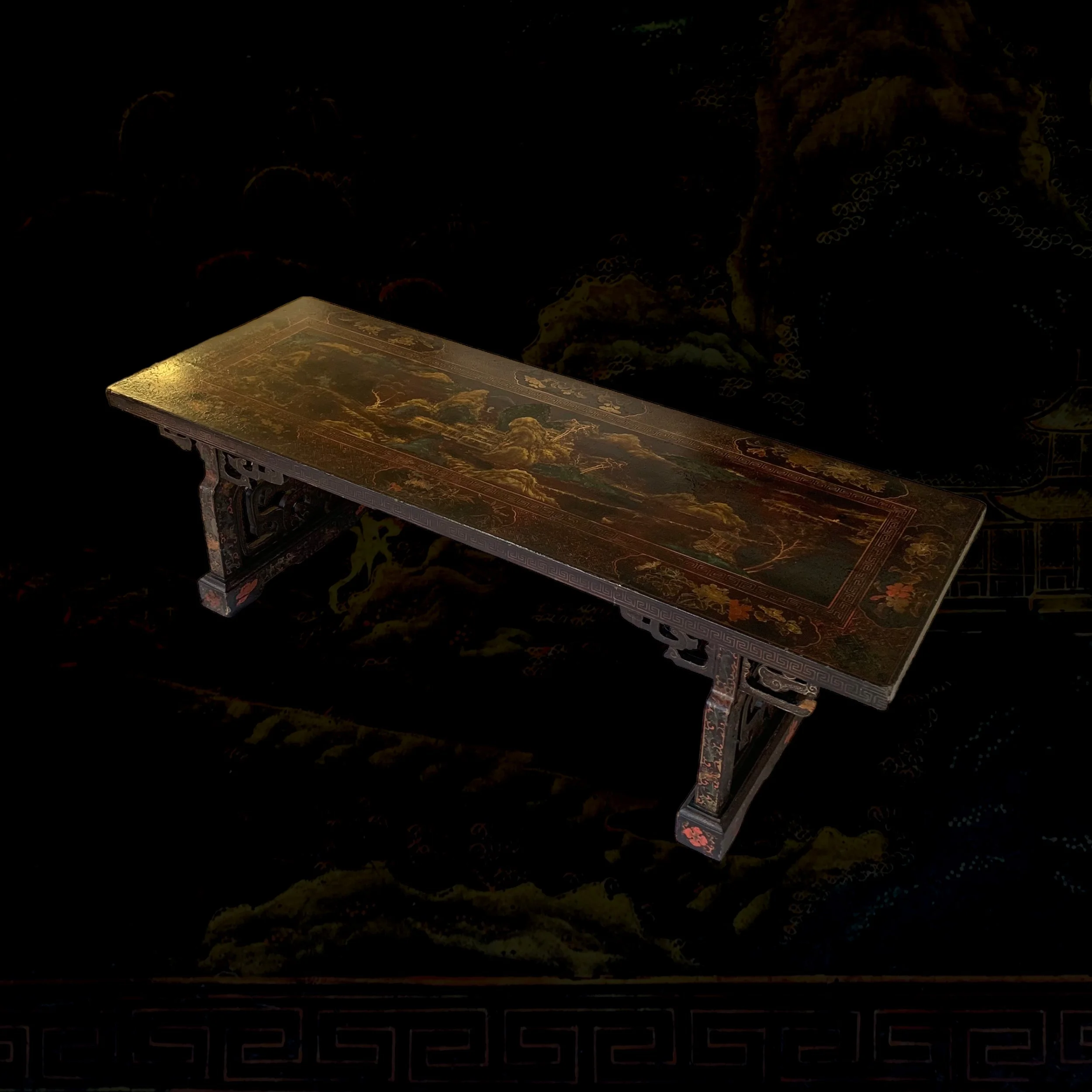 An ornate, dark wooden table with intricate carvings and a painted landscape scene on its surface, set against a mostly dark background.