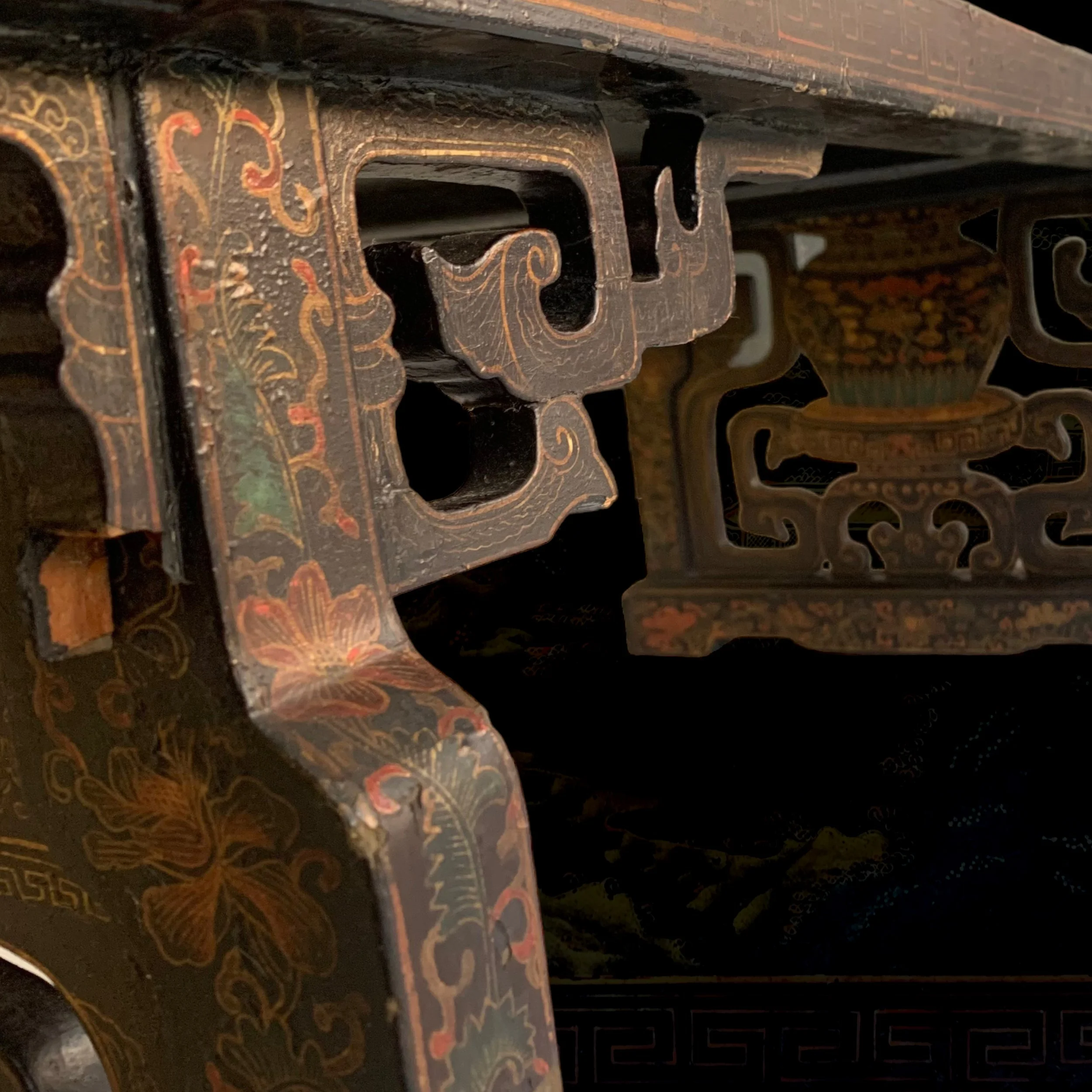 Close-up of an antique black lacquered furniture piece with intricate floral and scrollwork designs in red, gold, and green, featuring a small decorative shelf and detailed carving.