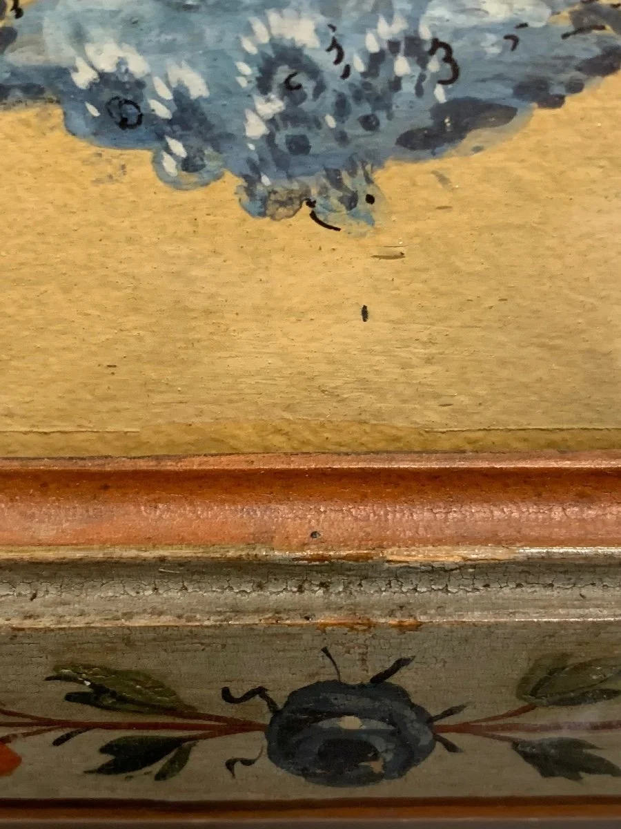 Close-up of decorative painted floral and insect designs on wooden furniture, including a blue flower or butterfly and a black bumblebee with leaves.